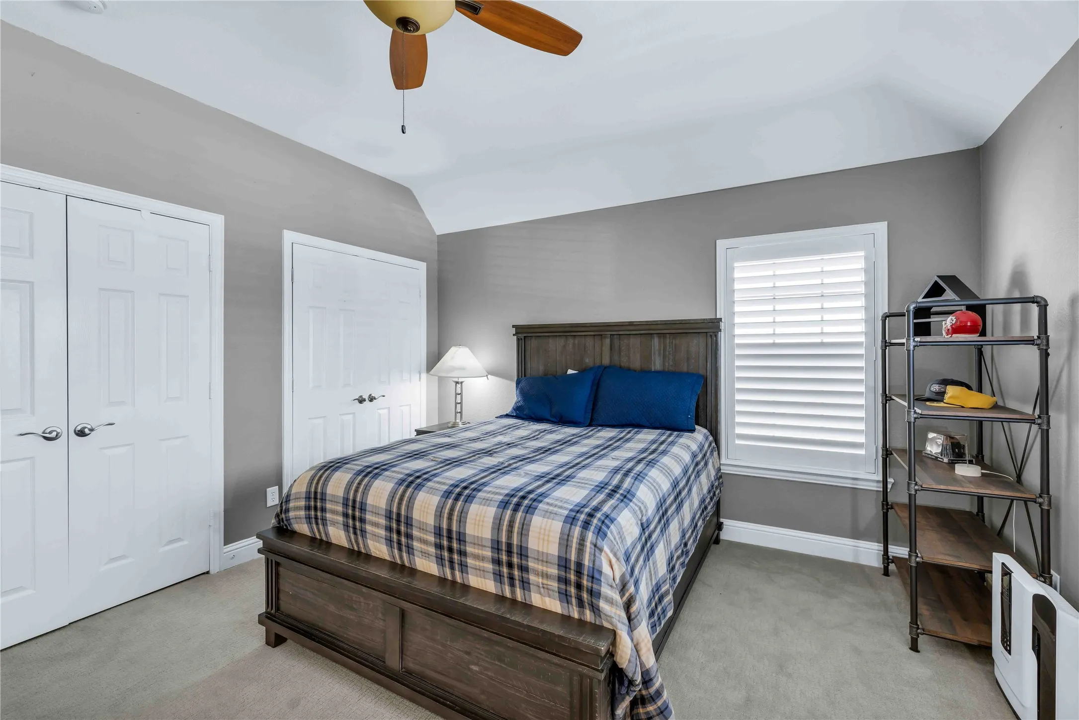 Bedroom featuring gray wall color, tray ceiling, carpeted flooring, and a window with white louvered shutters