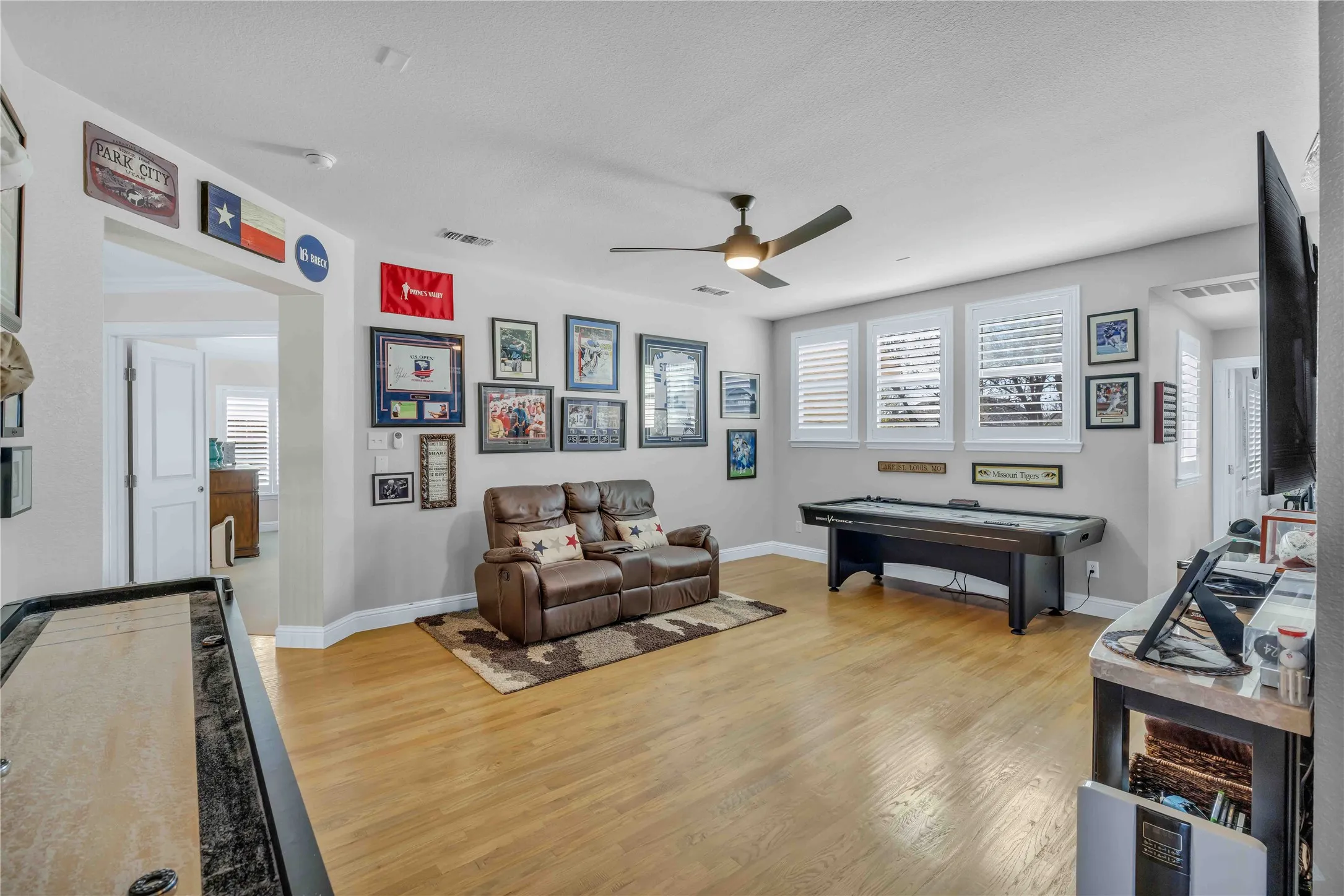 Spacious room featuring wood-finish flooring, a contemporary ceiling fan, and multiple windows with white plantation shutters