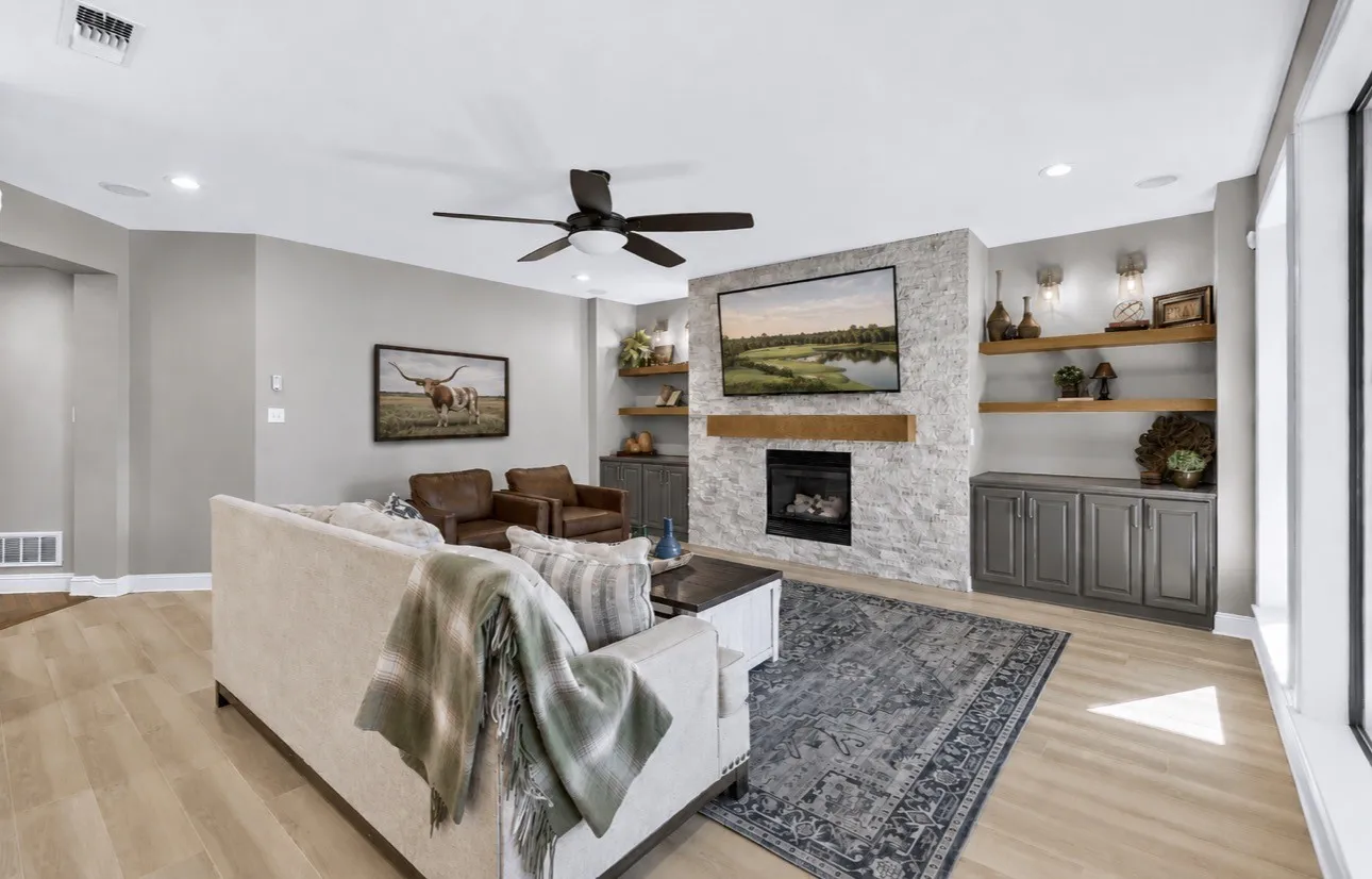 Living area featuring wood-finish flooring, a stone-clad fireplace with a wood mantel, and built-in shelving with integrated cabinetry