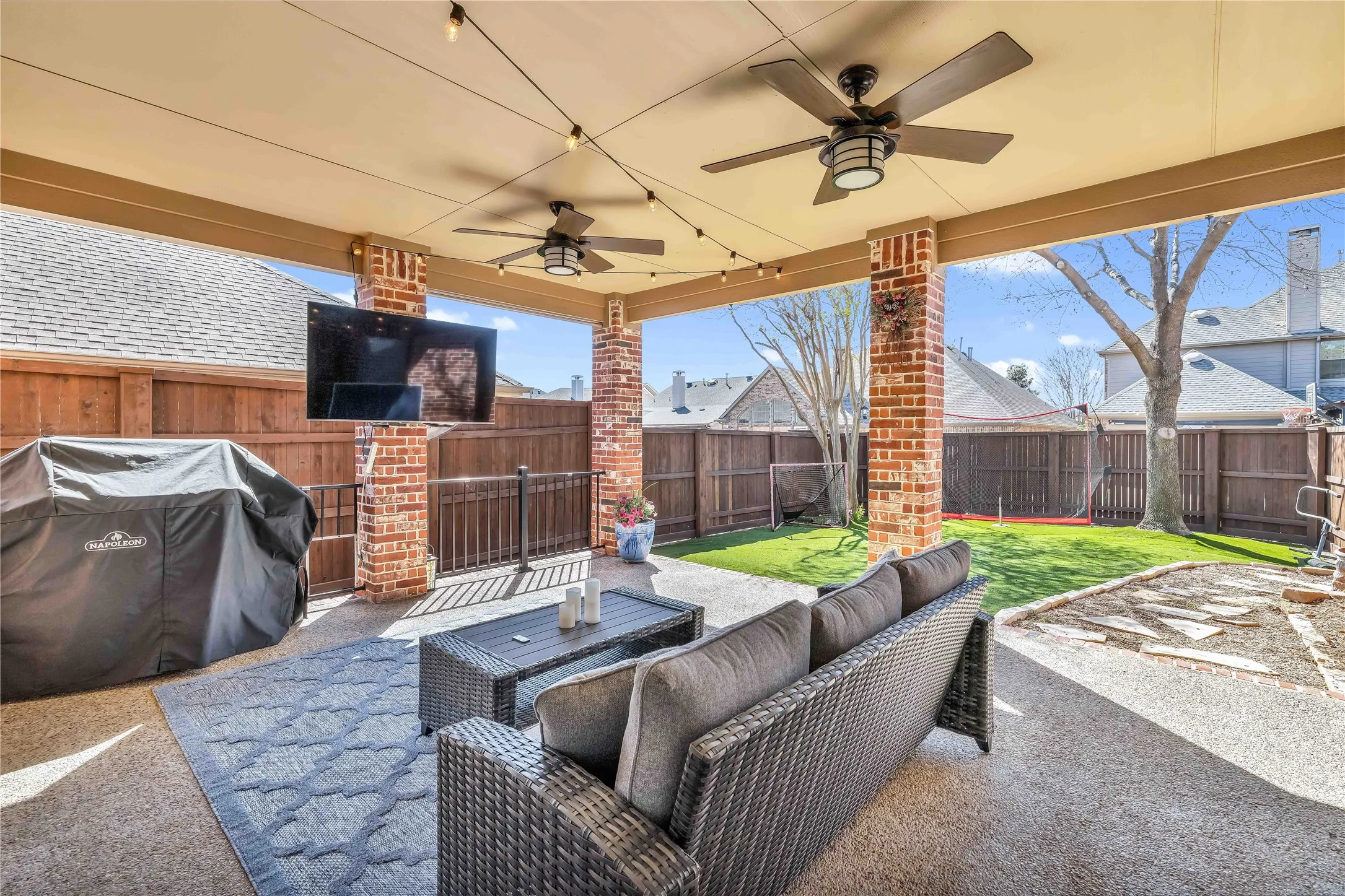 Covered patio featuring brick-clad columns, dual ceiling fans, string lighting, and an entertainment screen