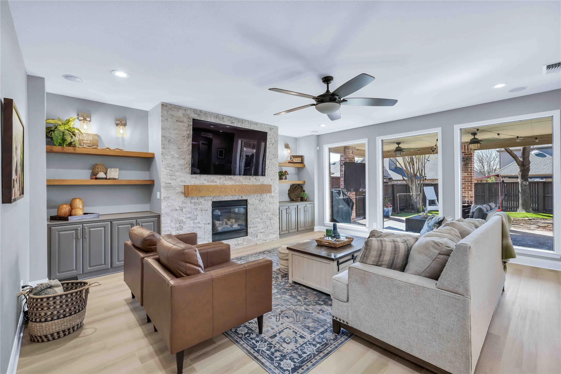 Living space featuring a stone-clad fireplace with built-in cabinetry, wood-finish flooring, recessed lighting, and a ceiling fan
