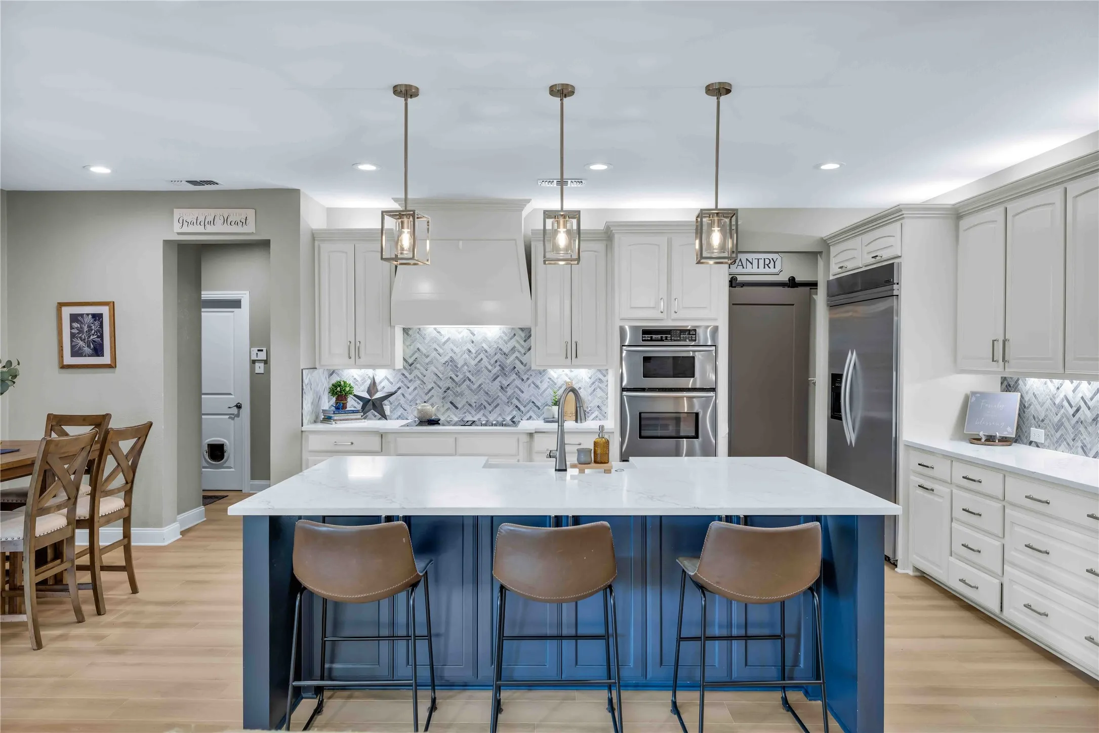Spacious kitchen featuring a central island with quartz countertop, light wood-finish flooring, white upper and lower cabinetry, stainless steel appliances, and a herringbone pattern tile backsplash