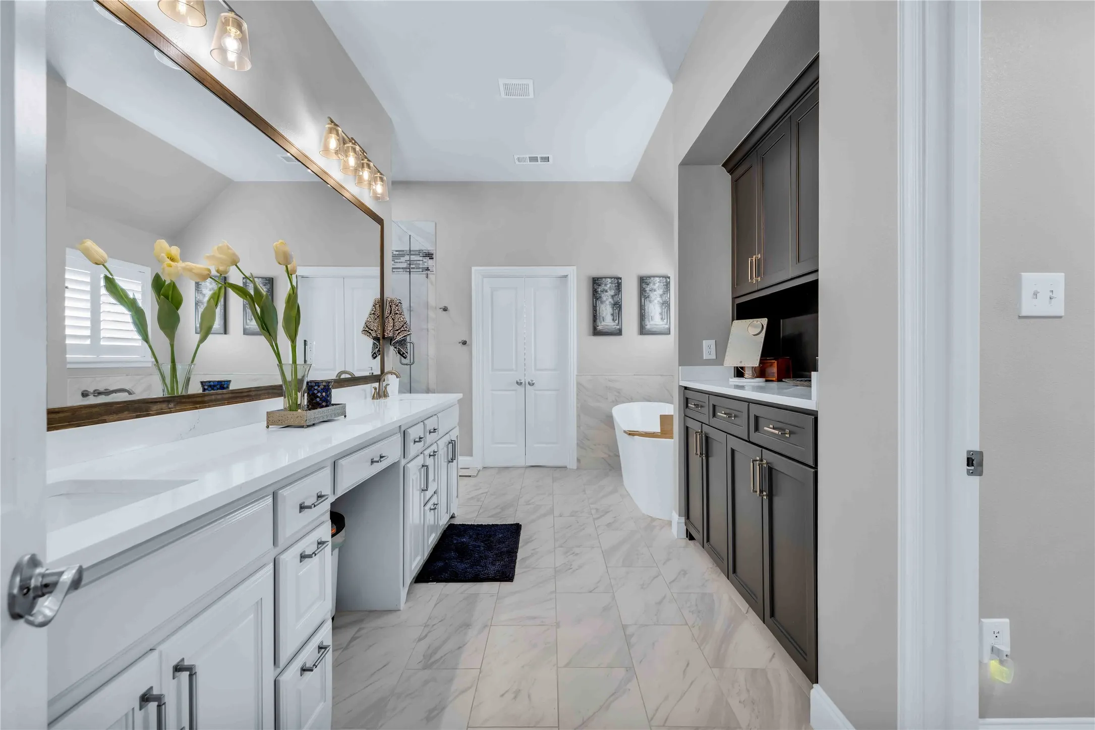 Bathroom featuring a dual vanity with white cabinetry and integrated sinks, a freestanding soaking tub, a glass-enclosed shower, a large wall-mounted mirror, and tile flooring