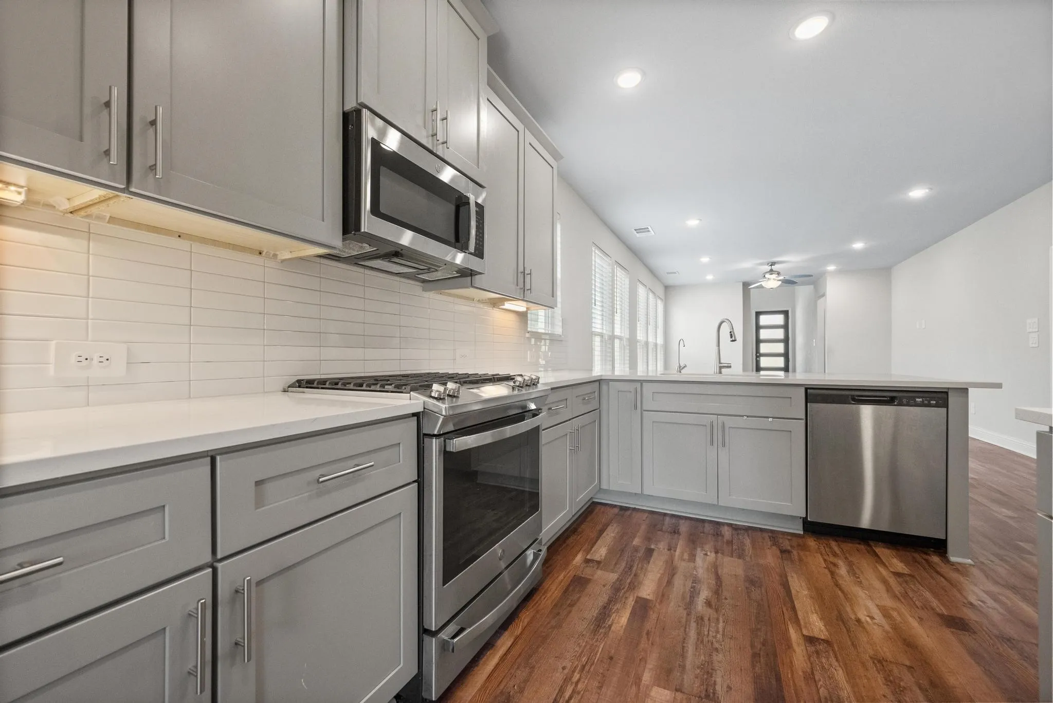 Modern kitchen featuring stainless steel appliances, grey cabinetry, white countertops, and a subway tile backsplash