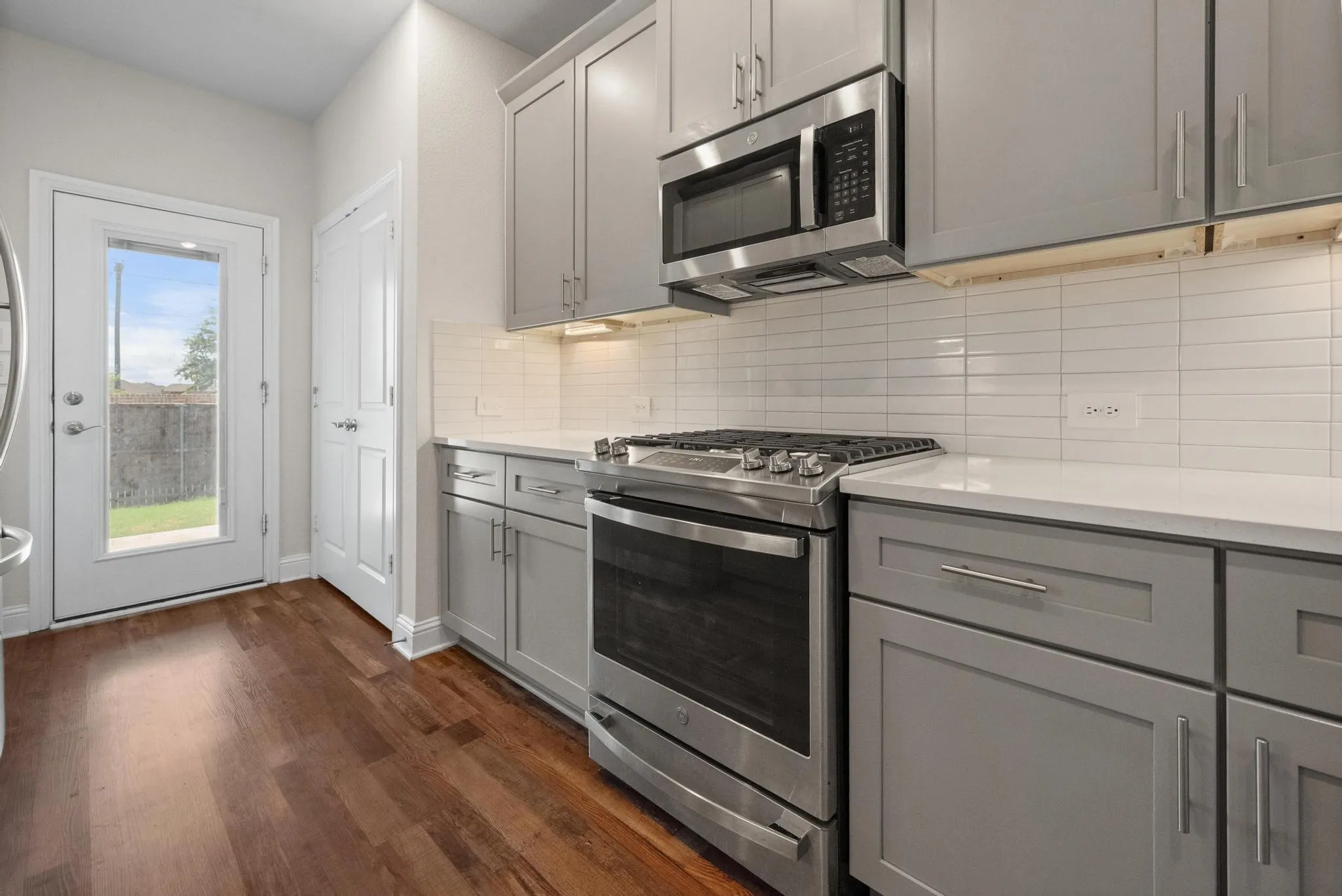 Kitchen featuring stainless steel appliances, light gray shaker cabinetry, white subway tile backsplash, and wood-finish flooring