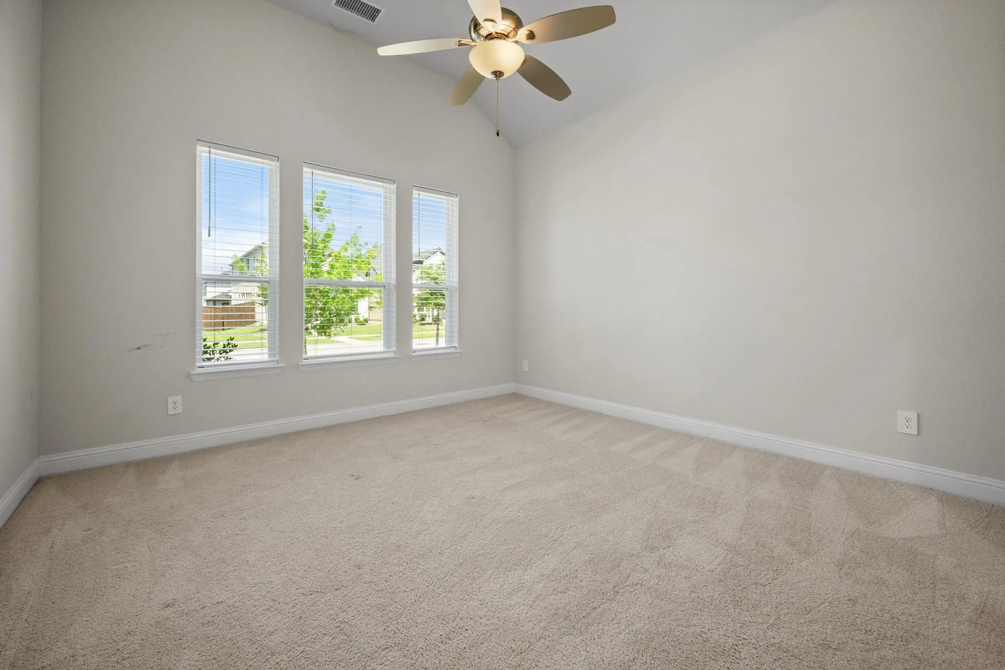 Carpeted room with a vaulted ceiling, three windows with blinds, a ceiling fan, and baseboard molding