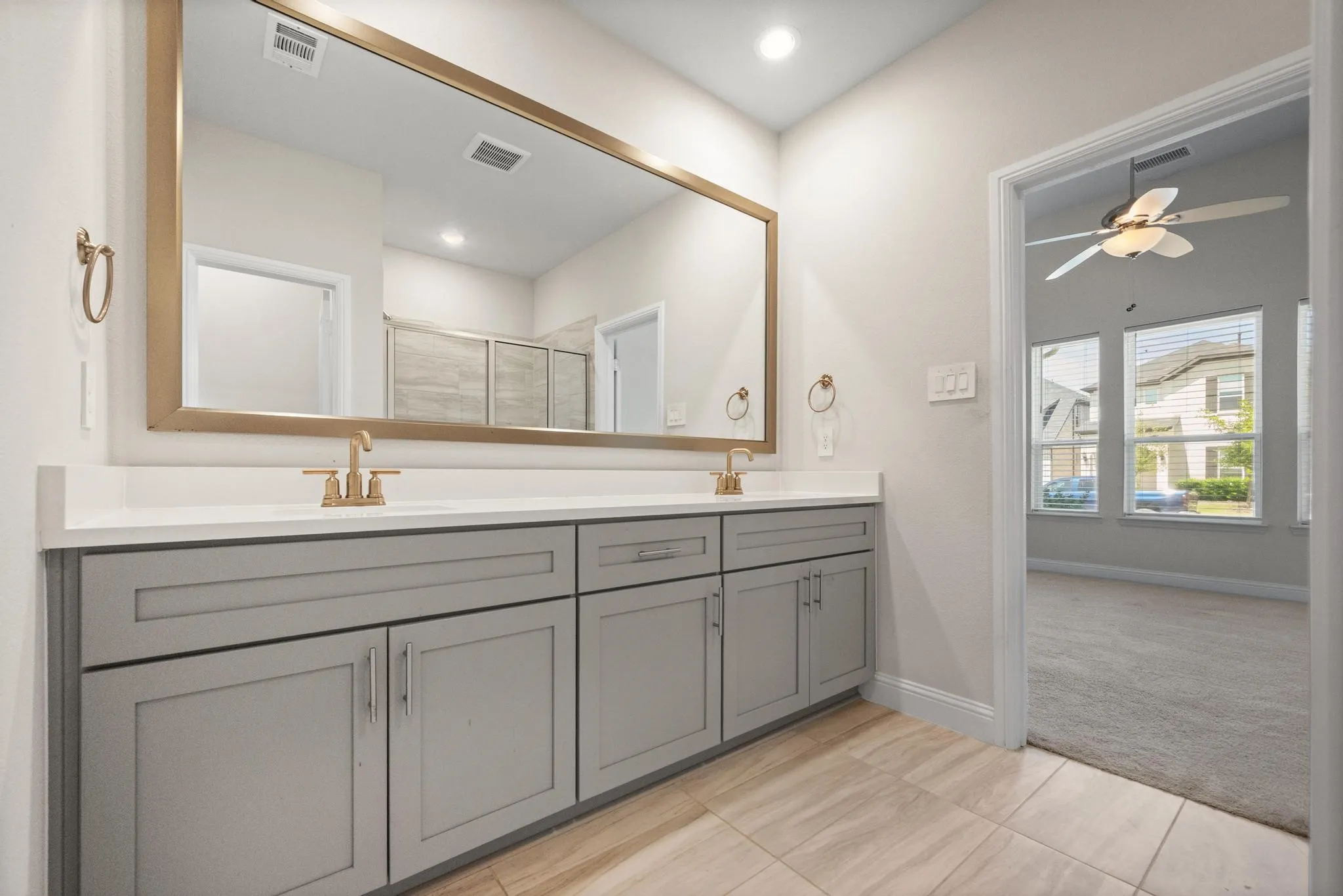 Dual vanity with light gray shaker-style cabinetry, white countertops, and gold-finish fixtures