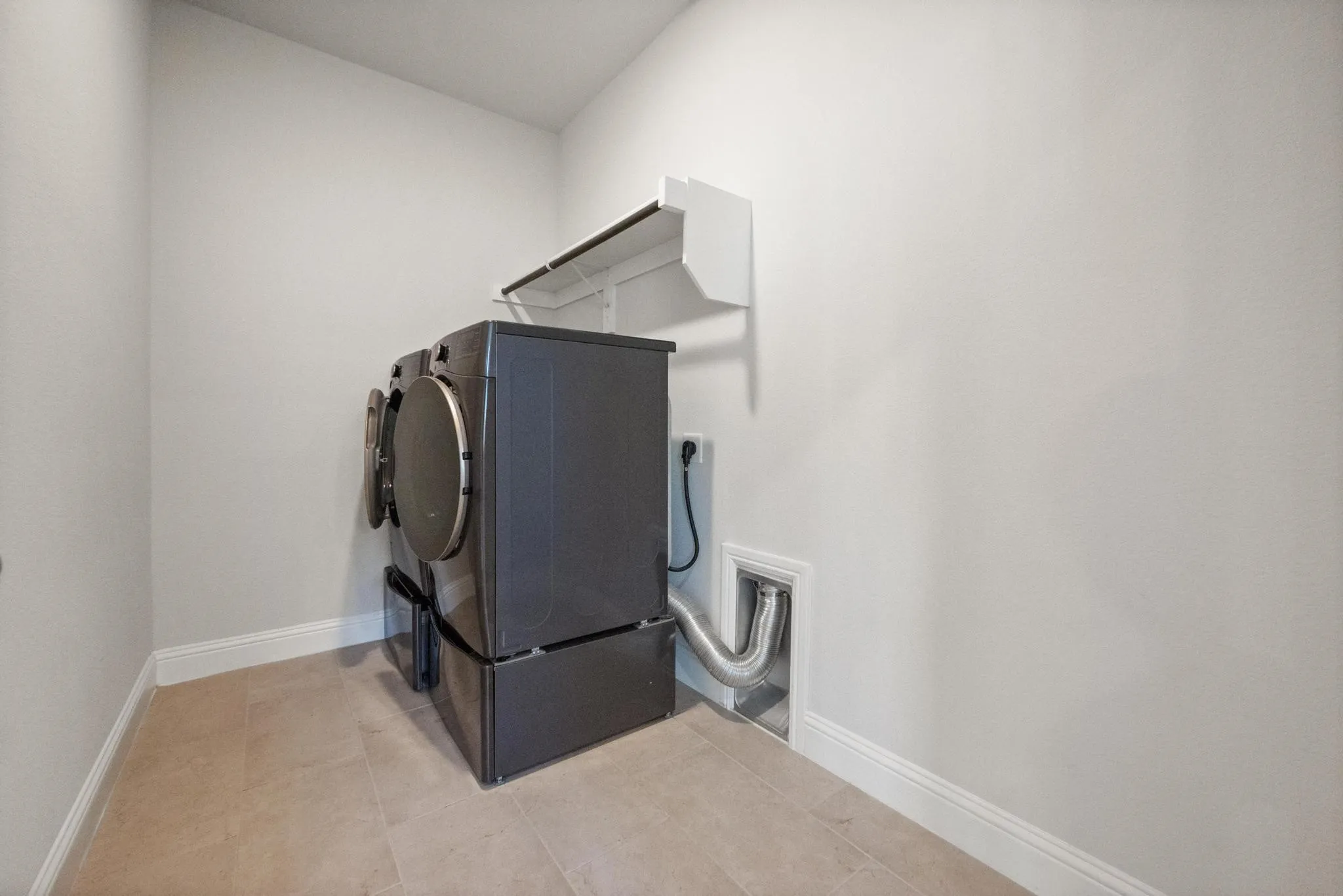 Utility room featuring light-toned flooring, white baseboards, and a white overhead shelf
