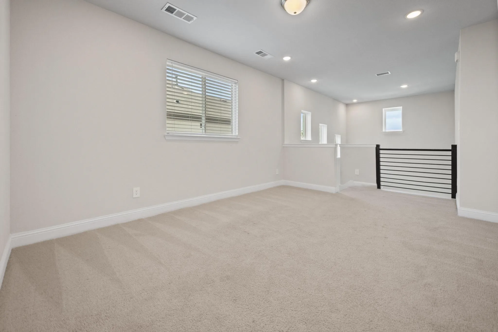 Spacious carpeted room featuring a ceiling light fixture, recessed lighting, and multiple windows