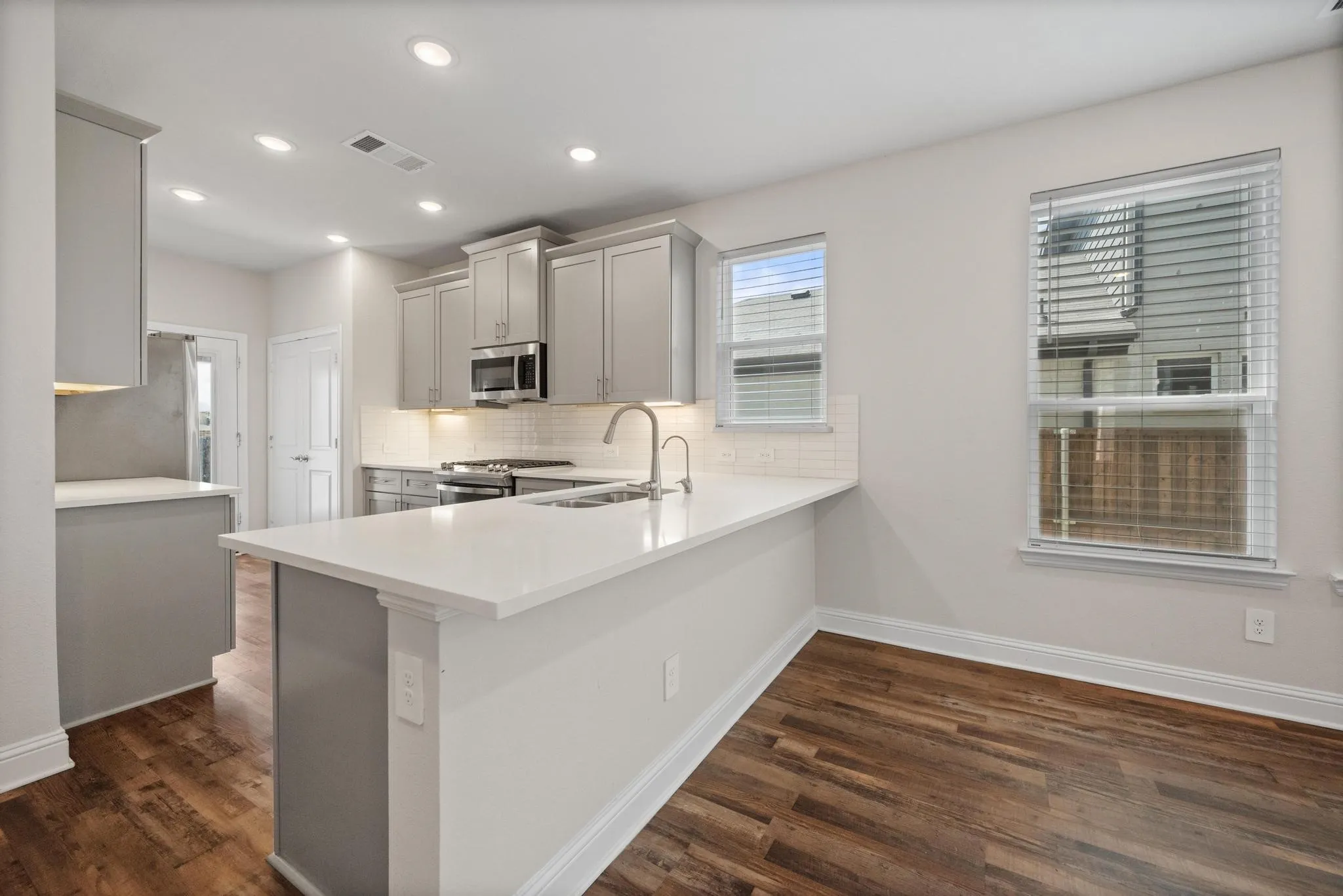 Kitchen featuring light gray cabinetry, stainless steel appliances, white subway tile backsplash, and wood-finish flooring