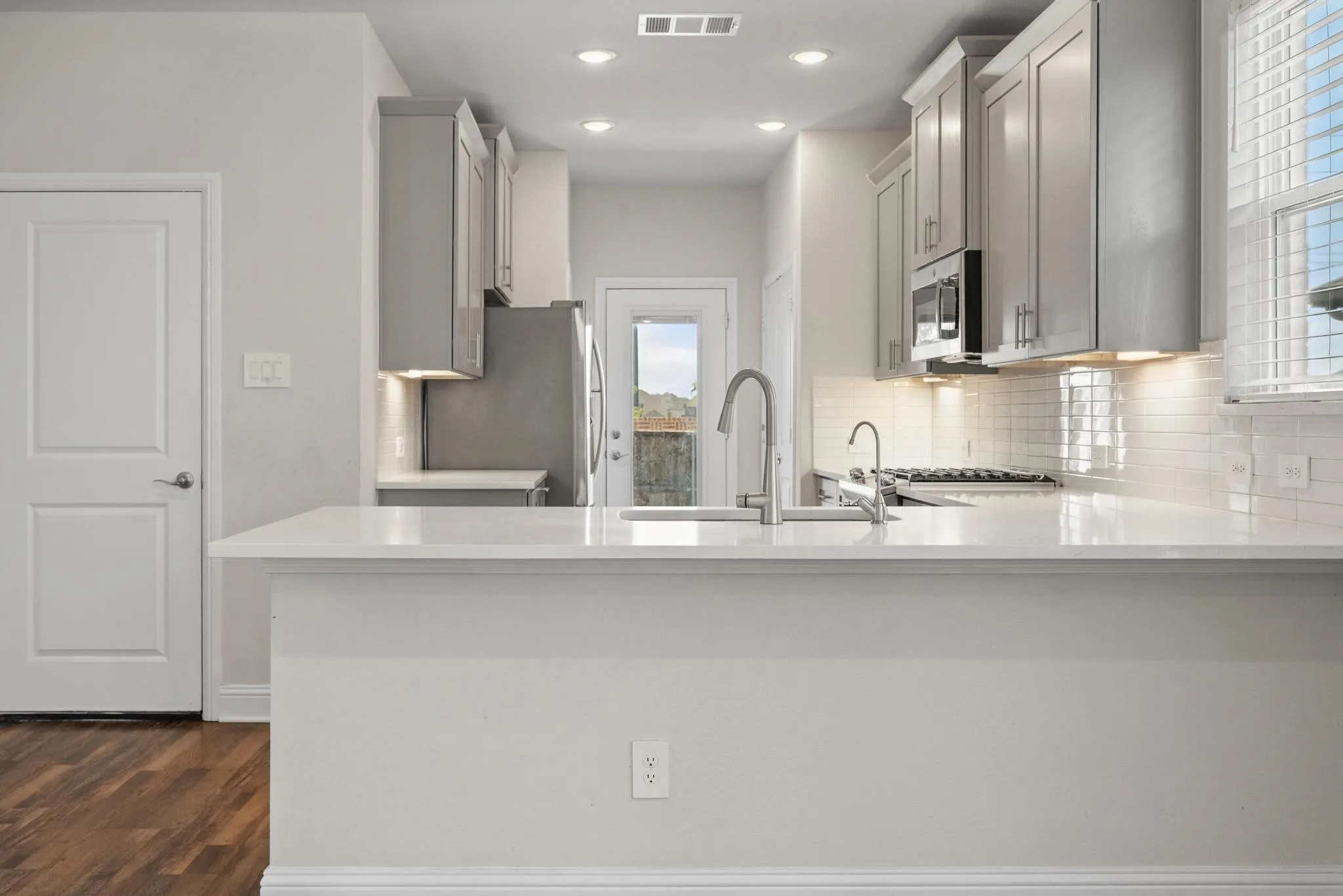 Modern kitchen featuring an extended white countertop peninsula, grey cabinetry, stainless steel appliances, and a tile backsplash
