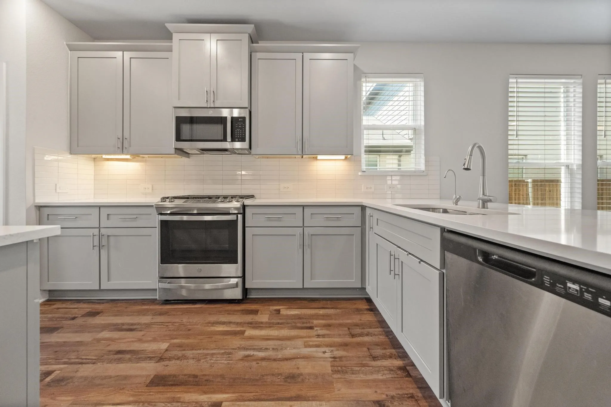 Modern kitchen featuring gray shaker-style cabinetry, stainless steel appliances, white subway tile backsplash, and wood-finish flooring