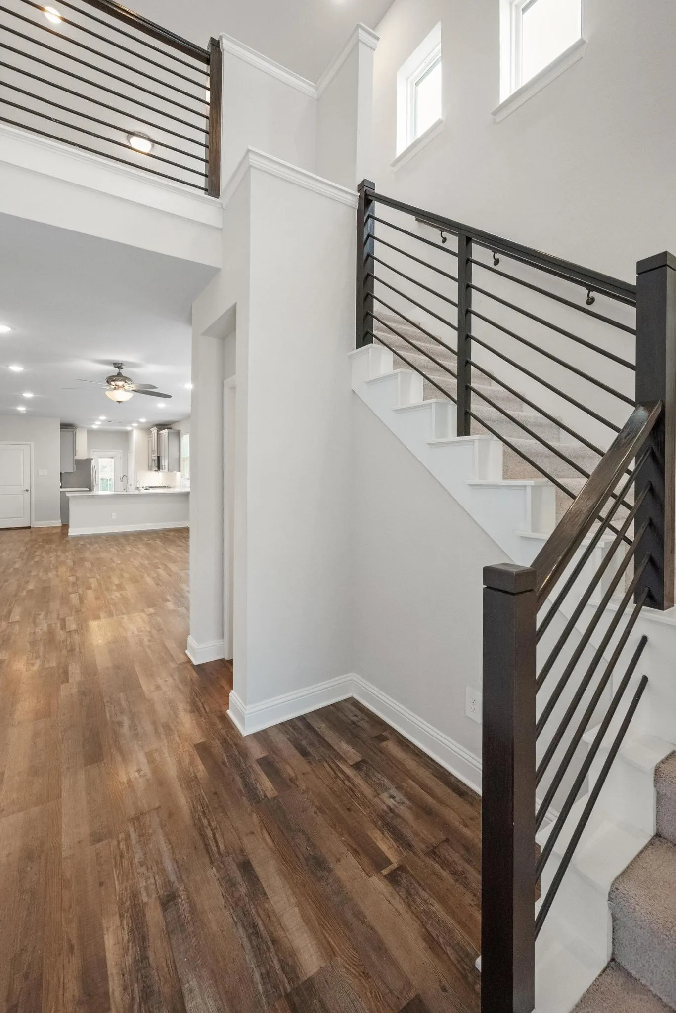 Modern staircase featuring horizontal metal railings, carpeted treads, and wood-finish flooring
