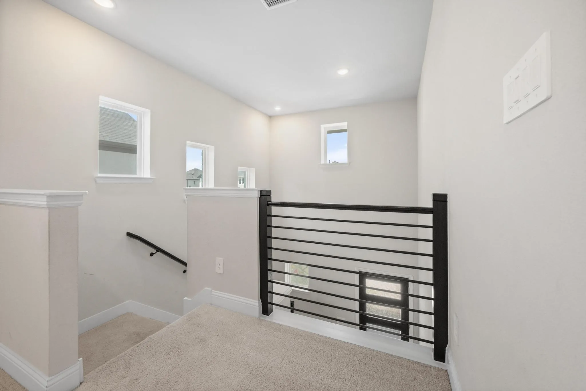 Second-story landing featuring a horizontal metal railing system and recessed lighting