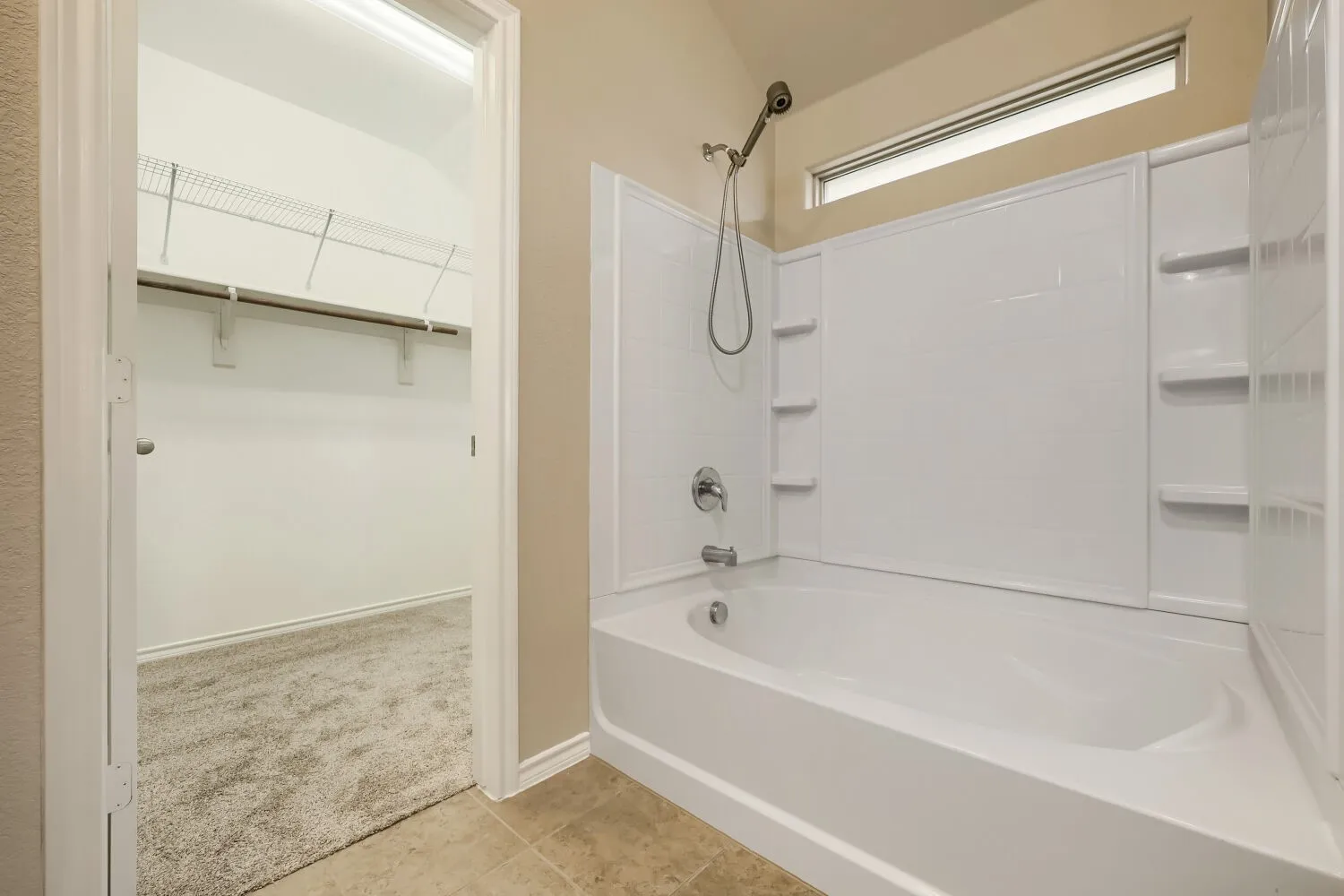 Bathroom featuring a white tub and shower combination with an integrated shelving unit, a chrome showerhead and faucet, and a high-set window