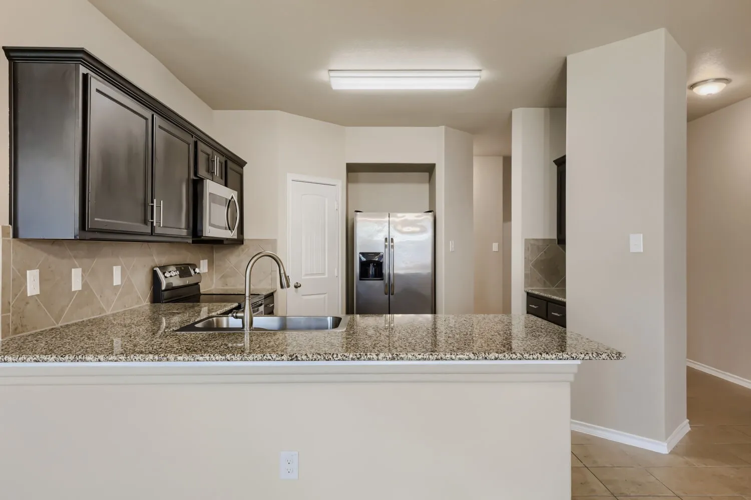 Kitchen featuring dark wood cabinetry, stainless steel appliances, a tile backsplash, granite countertops, and a stainless steel sink with a high-arch faucet