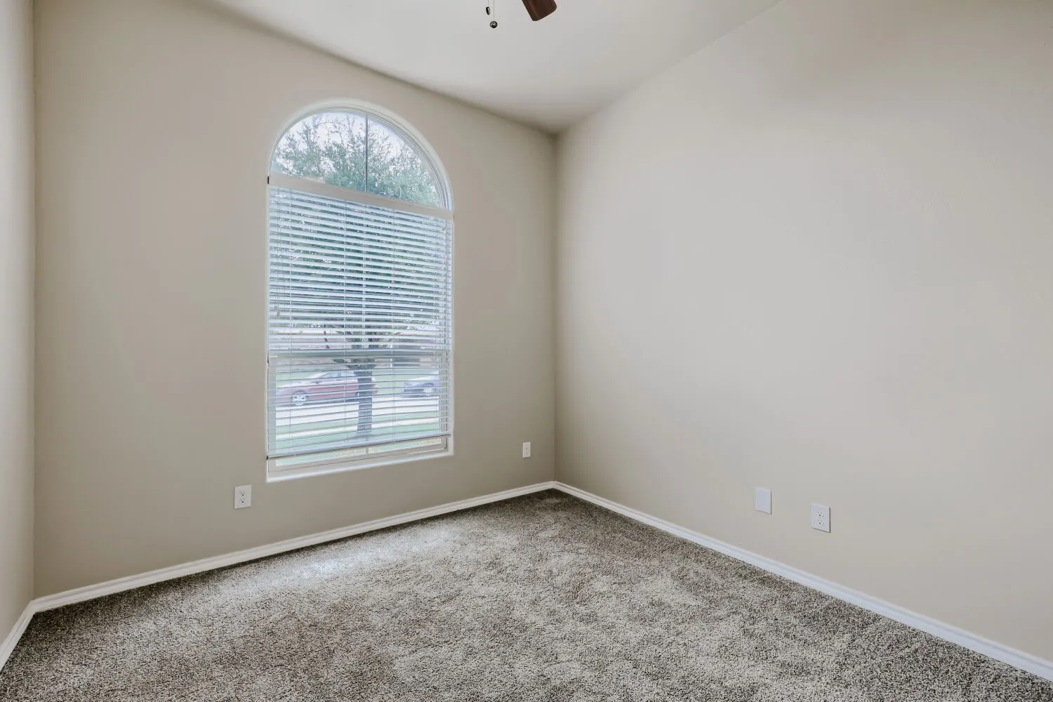 Spacious room featuring a prominent arched window with blinds, vaulted ceilings, neutral-toned walls, and plush carpet flooring