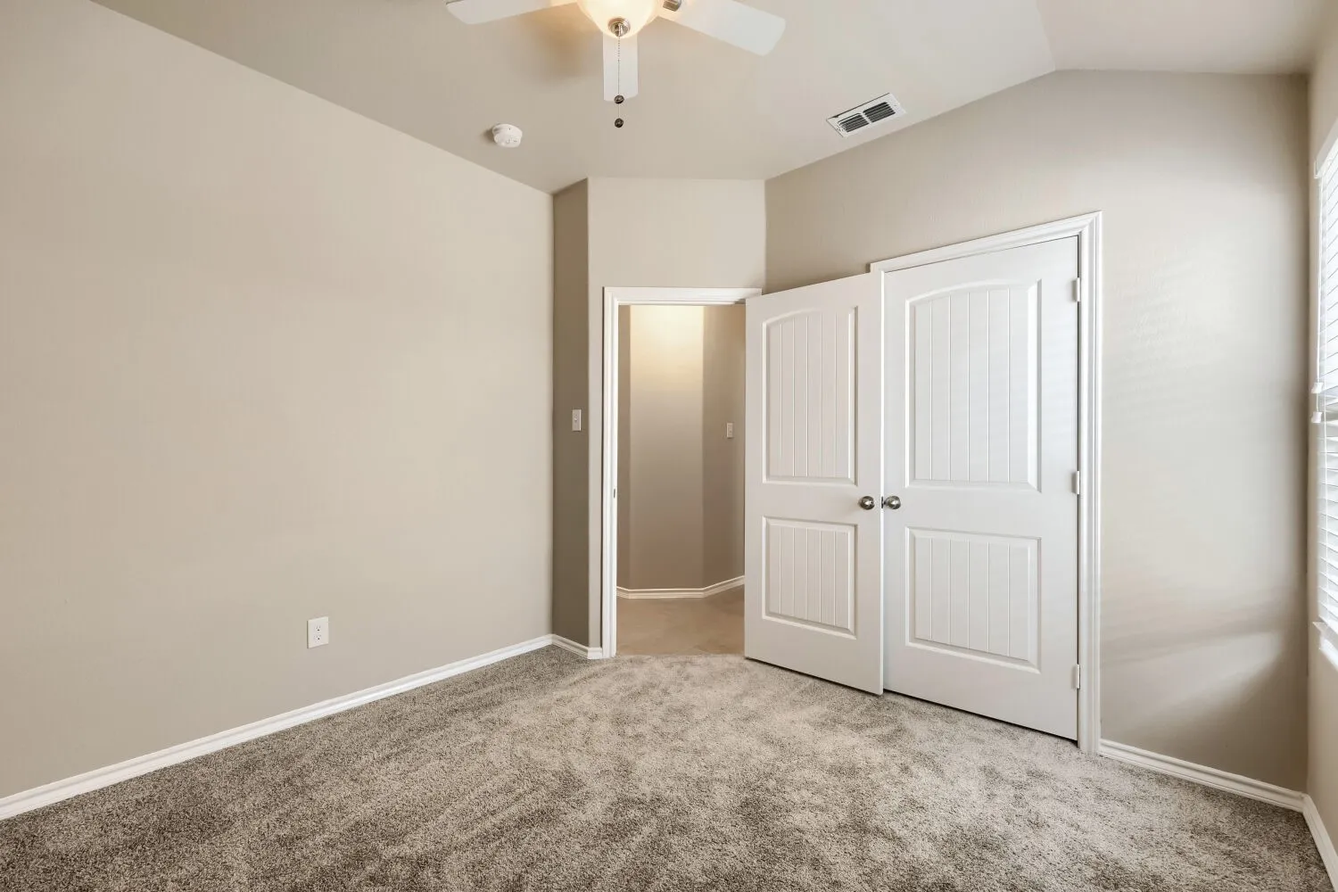 Room featuring neutral-toned walls, textured carpet flooring, and a ceiling fan with integrated lighting