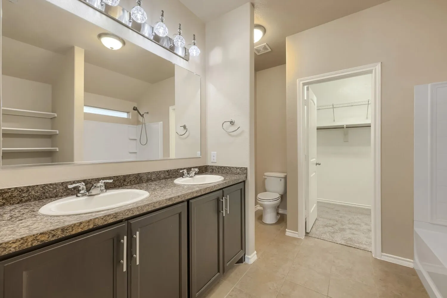 Spa-inspired master bathroom featuring a dual-sink vanity with dark cabinetry, granite countertop, and polished chrome fixtures