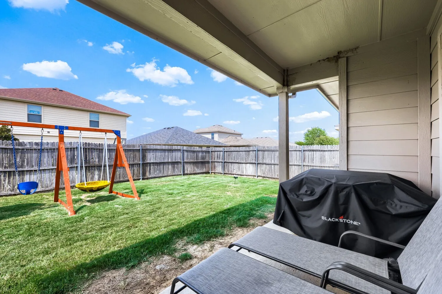 Covered patio with concrete slab overlooking a fenced grassy yard