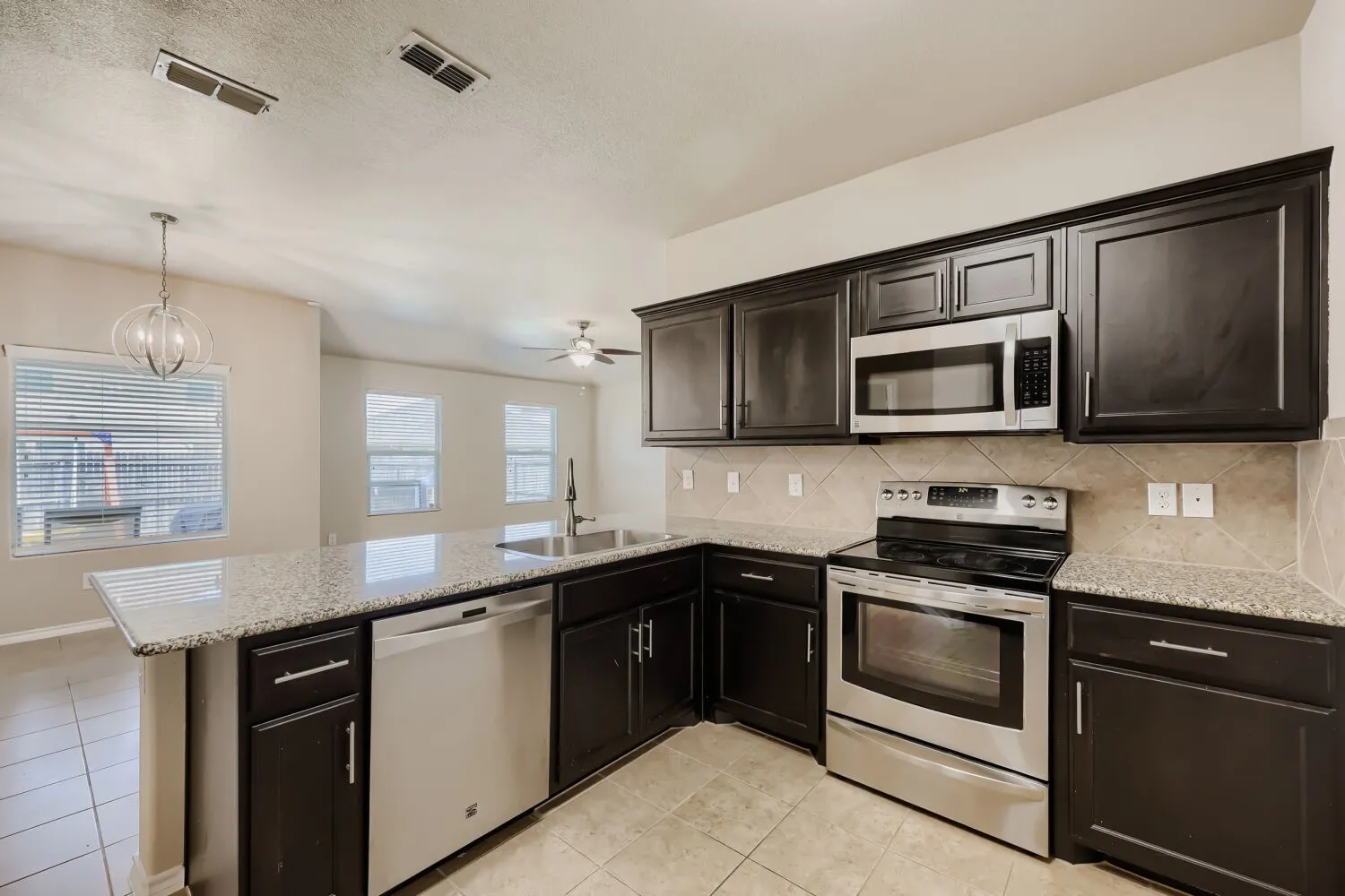 Kitchen featuring dark cabinetry, granite-finish countertops, stainless steel appliances, and a tiled backsplash