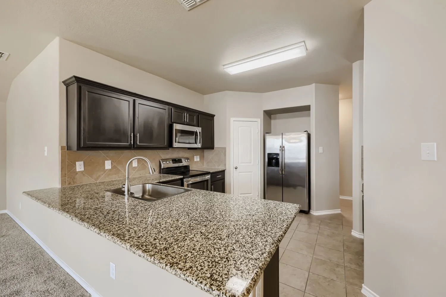 Kitchen featuring granite countertops, dark wood-finish cabinetry, stainless steel appliances, and a tile backsplash