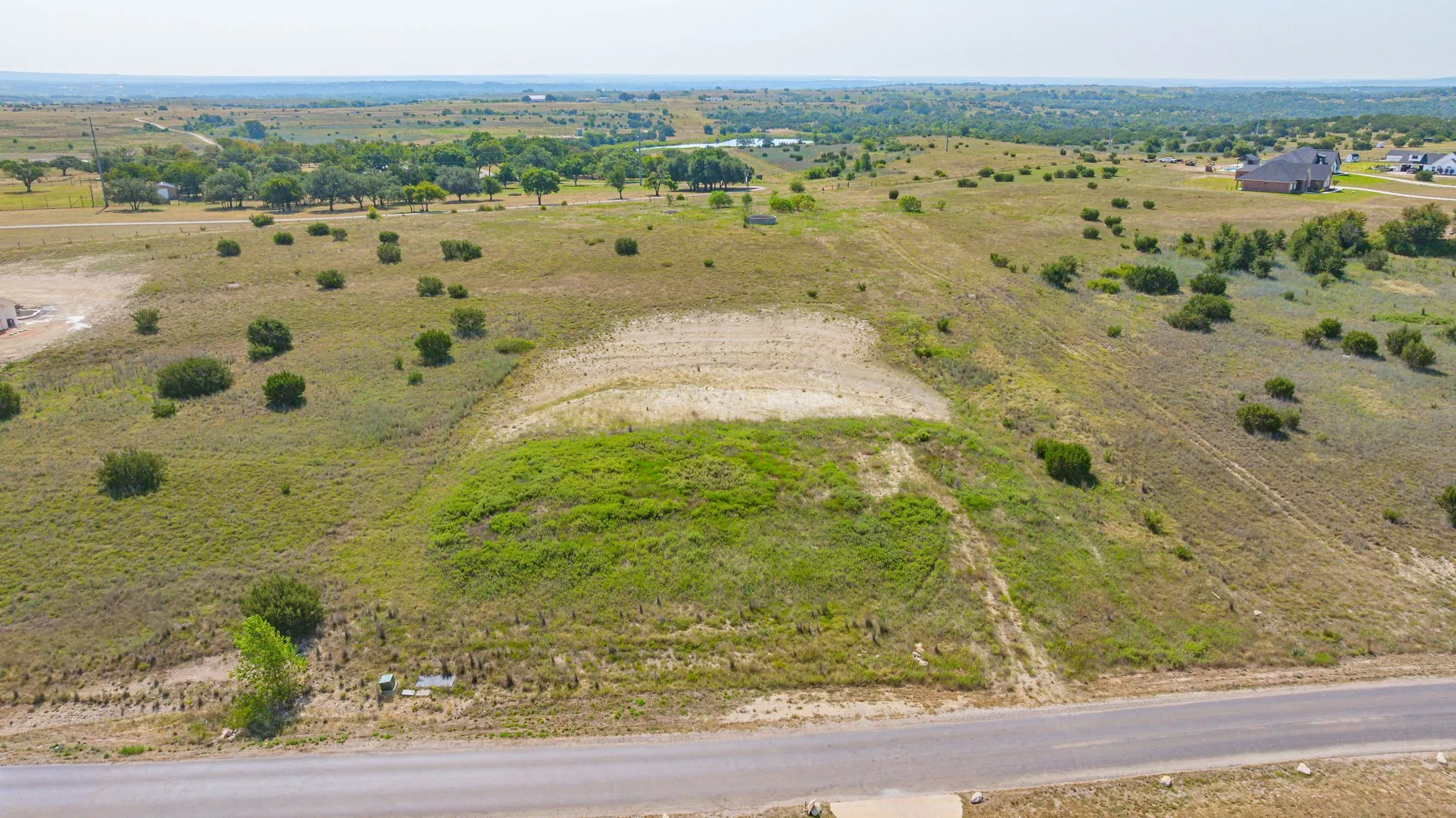 Expansive undeveloped land featuring a paved road frontage, natural vegetation, and distant tree lines