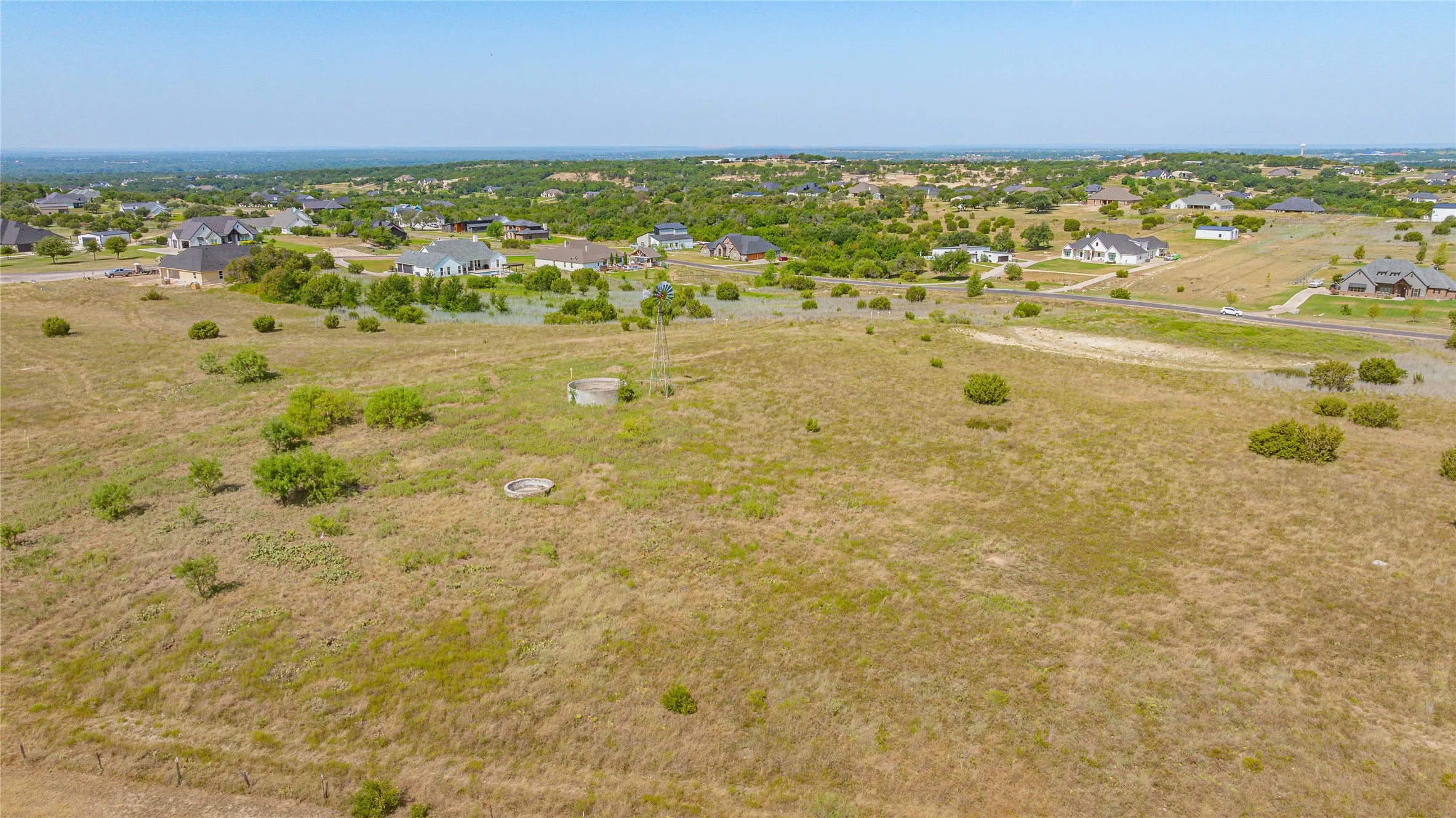 Expansive rural property featuring a windmill, scattered low-lying trees, and a distant residential area