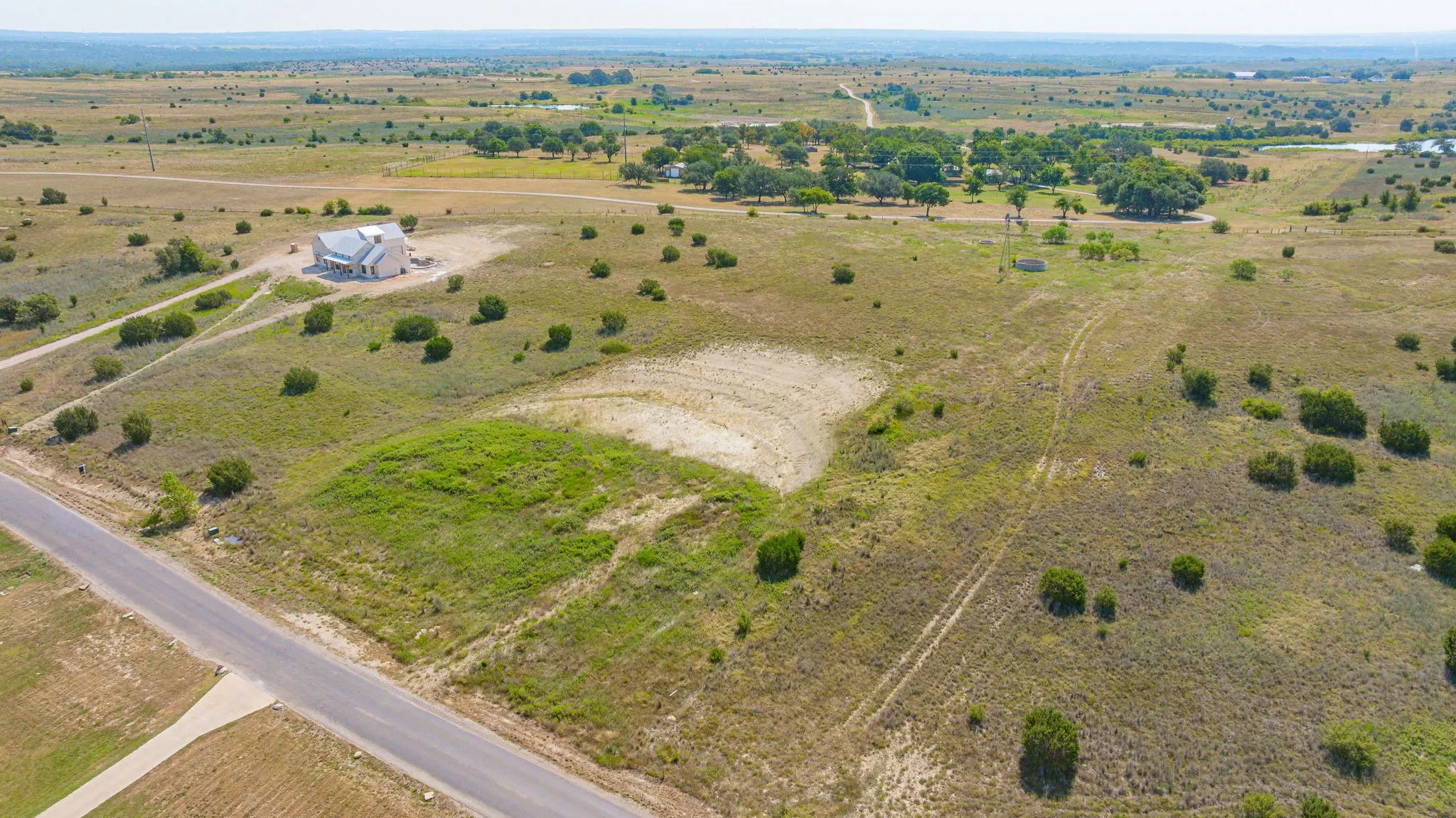 Expansive rural acreage featuring gently rolling pastureland with scattered mature oak trees, paved road frontage, and a modern residence situated on the property