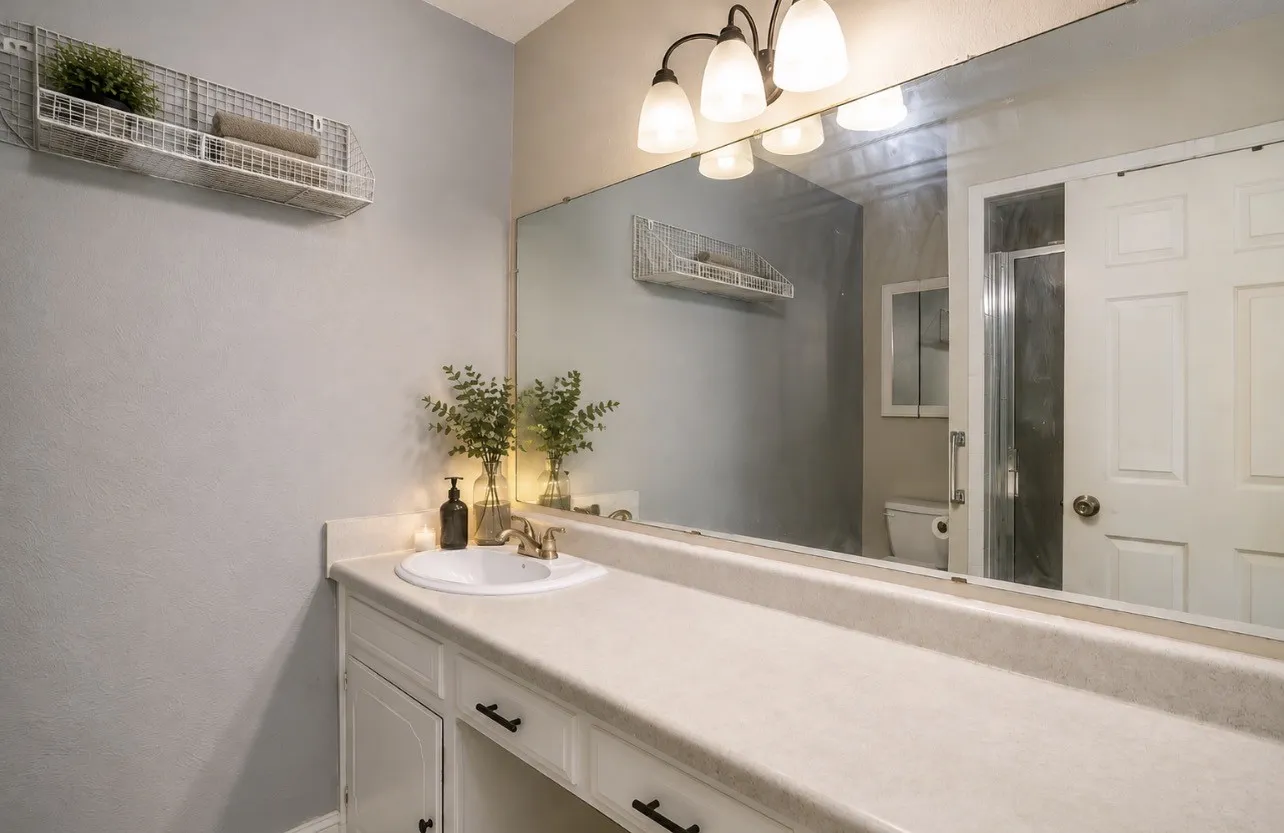 Virtually staged. Single vanity with integrated sink, expansive mirror, and overhead light fixture
