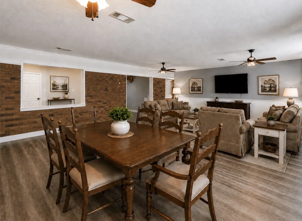 Virtually staged. Open-concept dining and living space featuring wood-finish flooring, brick accent walls, and ceiling fans