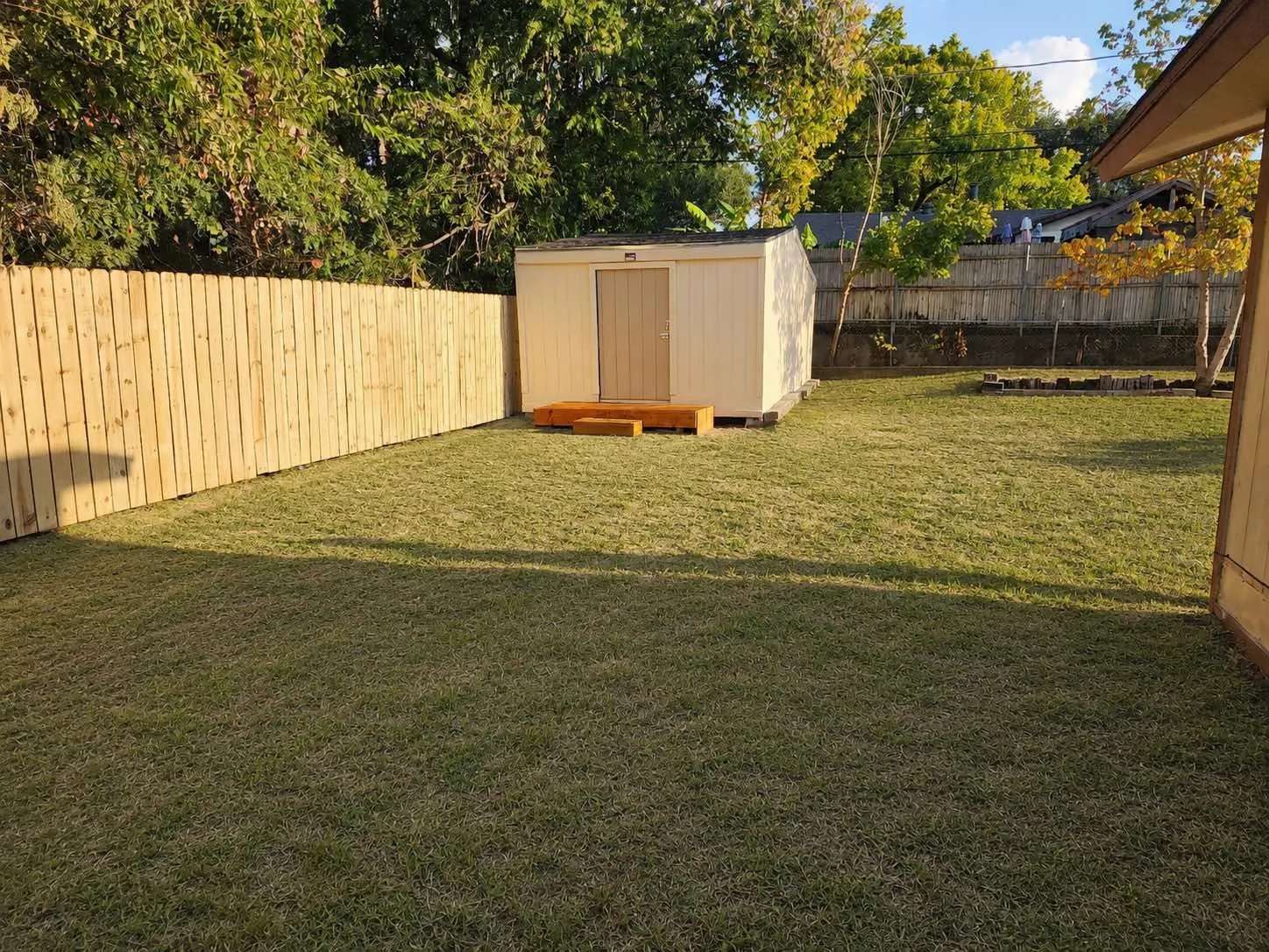 Expansive lawn area featuring a newly installed privacy fence, a detached storage shed with a small wood-finish deck, and mature trees bordering the property