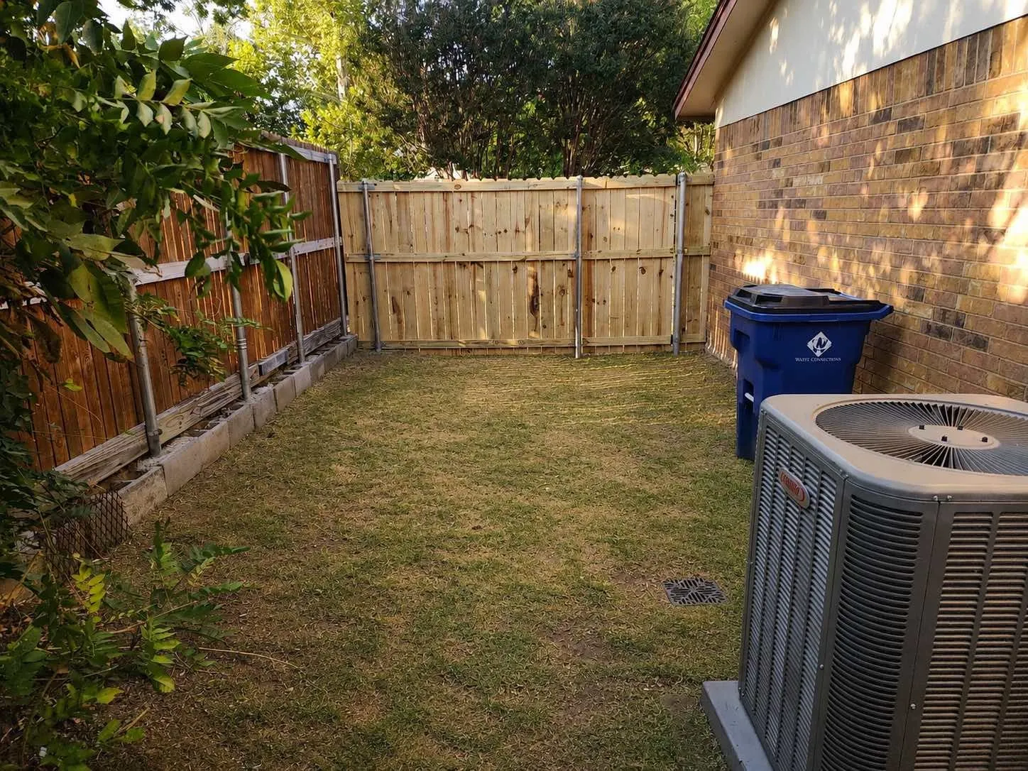 Enclosed yard space with a wood privacy fence, a brick exterior wall, and an outdoor HVAC unit on a concrete pad
