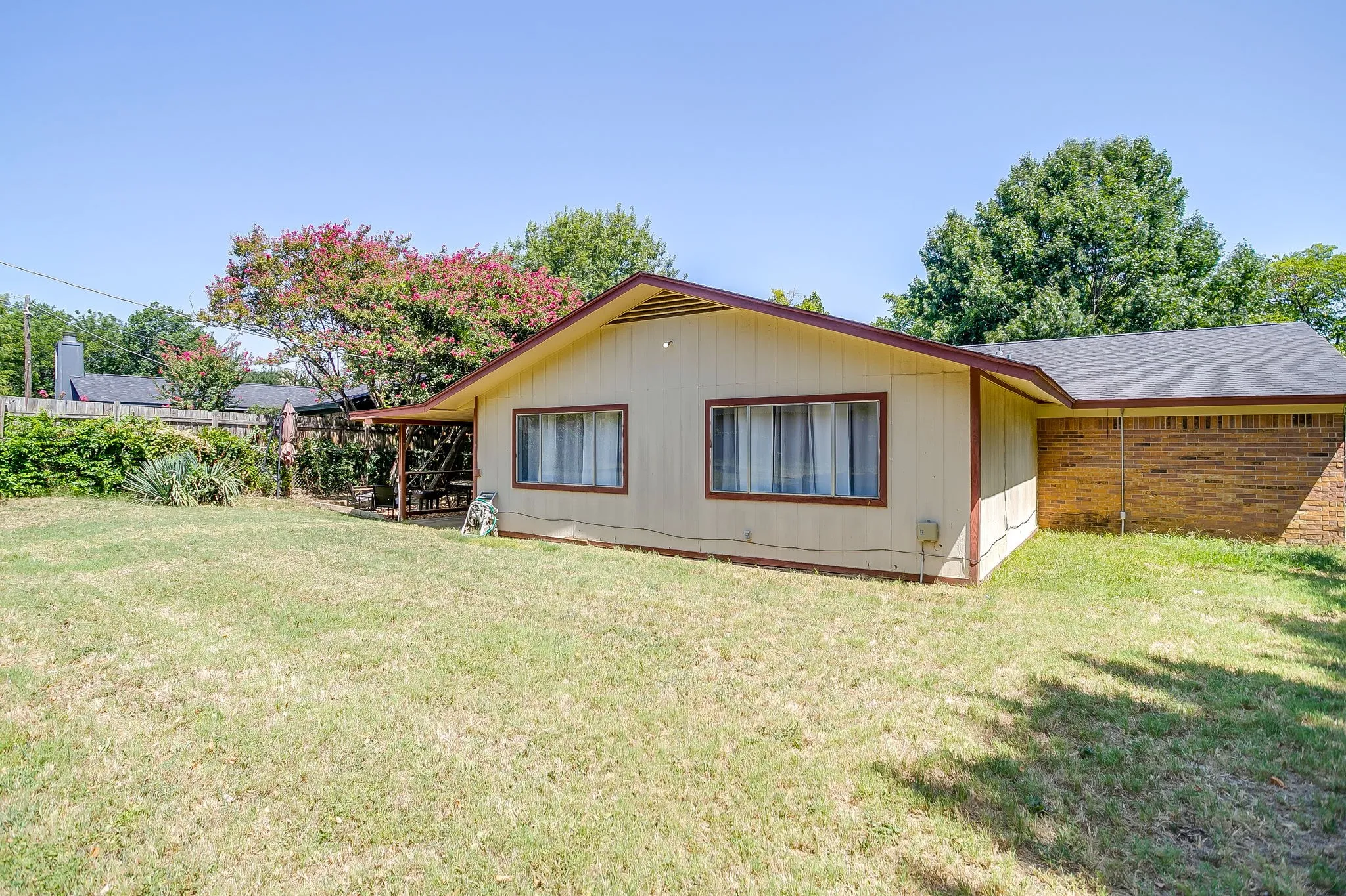 Expansive rear yard featuring a covered patio, mature trees, and a wooden privacy fence