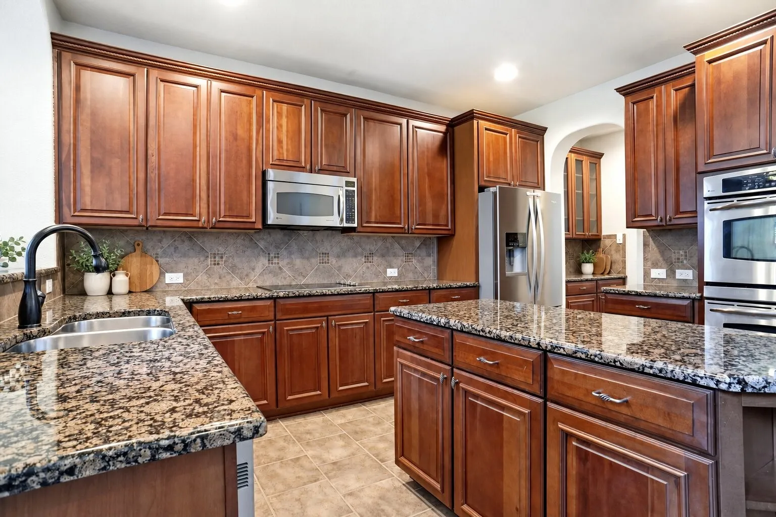 Spacious kitchen featuring abundant wood cabinetry, granite countertops, a large center island with additional storage, stainless steel appliances, and double ovens. Photos have been AI enhanced for presentation; no material property features were altered.