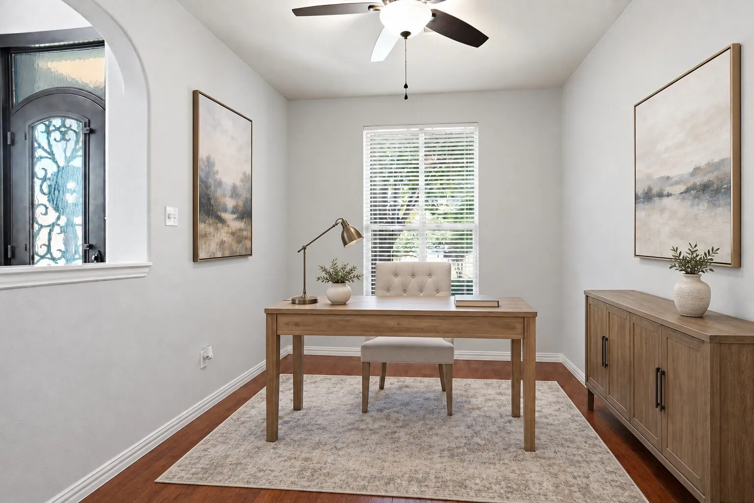 Private home office featuring built-in shelving, wood flooring, abundant natural light, and convenient placement just off the entry foyer. Furniture edited out of photo. Photos have been AI enhanced for presentation; no material property features were altered.
