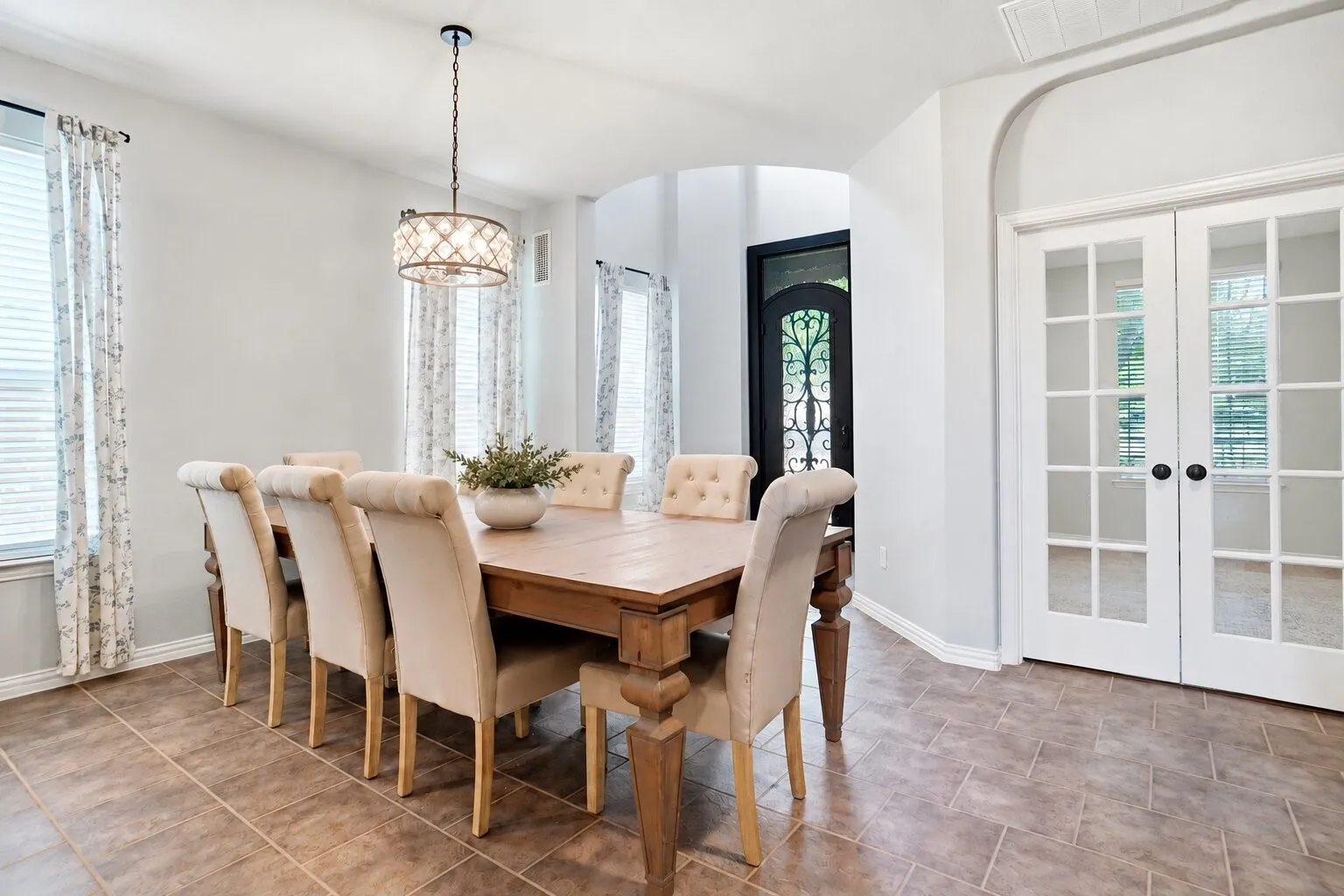Spacious formal dining room featuring abundant natural light, a decorative chandelier, tile flooring, and French doors leading to the private home office. Photos have been AI enhanced for presentation; no material property features were altered.