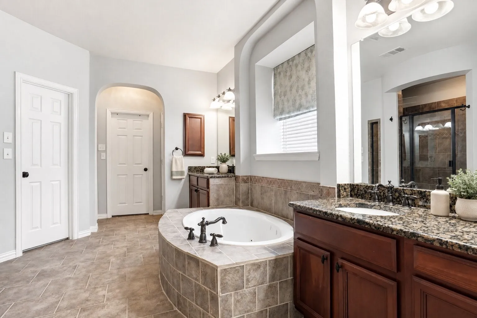 Spacious primary bathroom featuring dual vanities with granite countertops, a large soaking tub, separate walk-in shower, and two separate closets. Photos have been AI enhanced for presentation; no material property features were altered.