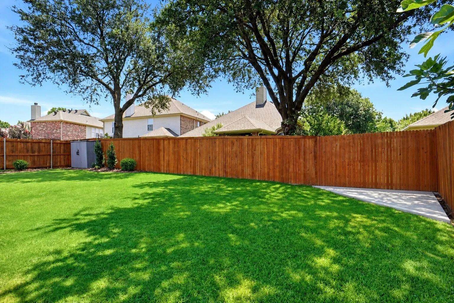 Spacious backyard with a large grassy lawn, mature shade trees, updated landscaping, and easy access to the pergola-covered outdoor living area. Additional slab poured in the corner is perfect for storage or a future fire pit. Photos have been AI enhanced for presentation; no material property features were altered.