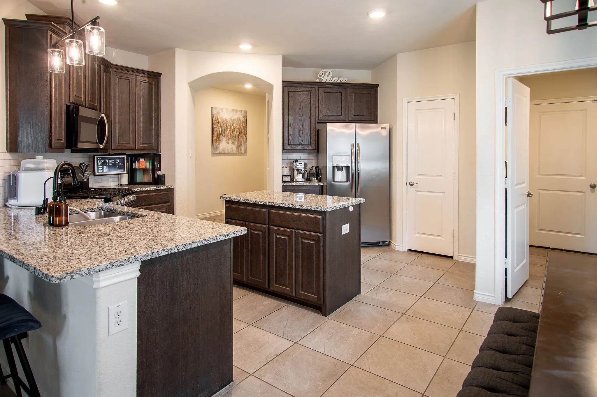Kitchen featuring dark wood-finish cabinetry, light speckled countertops, a center island with additional cabinetry, stainless steel appliances, and tile flooring