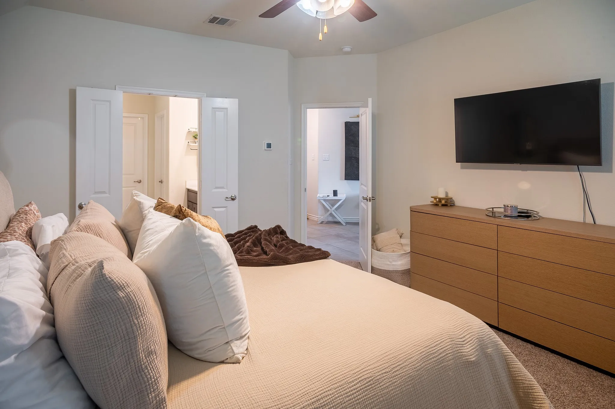 Bedroom featuring a ceiling fan, light-toned carpeting, and a wall-mounted television