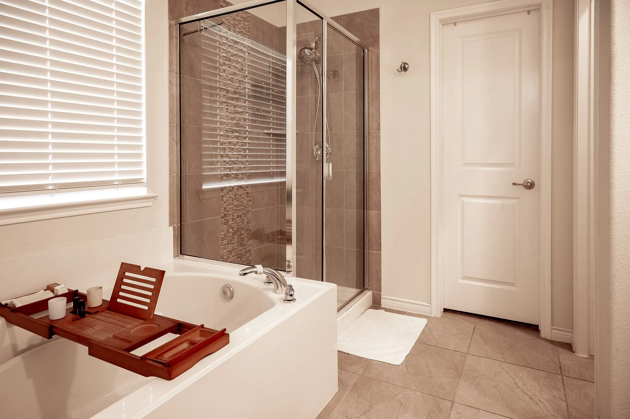 Spacious bathroom featuring a built-in soaking tub with deck-mounted chrome fixtures, a glass-enclosed shower with tile surround and decorative accent, and neutral tile flooring
