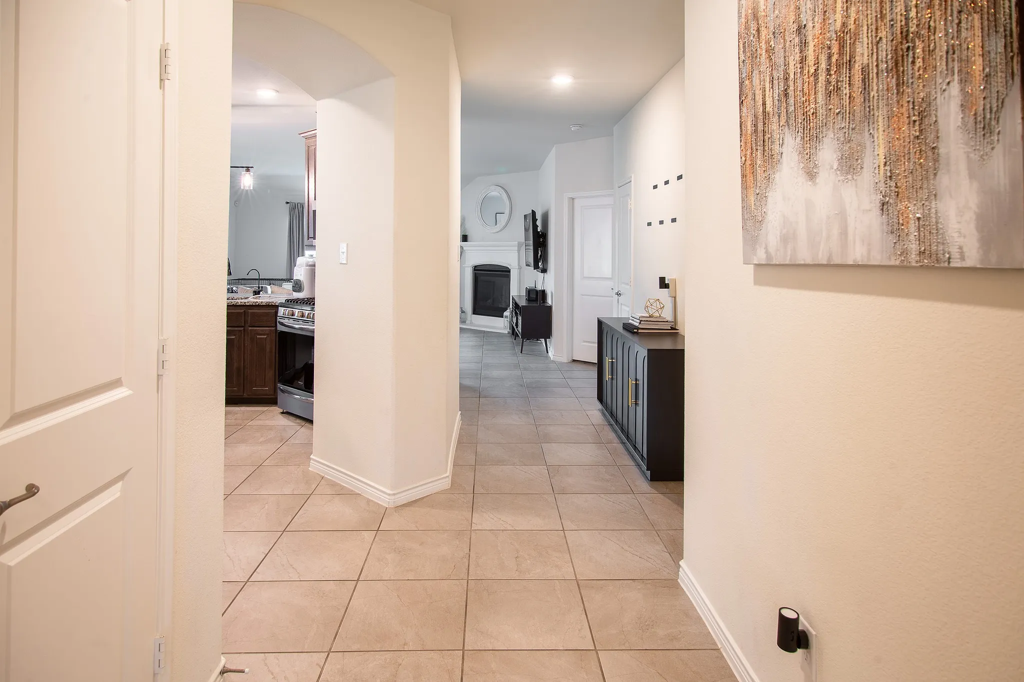 Interior hallway with light-toned tile flooring, archway detailing, and white baseboards