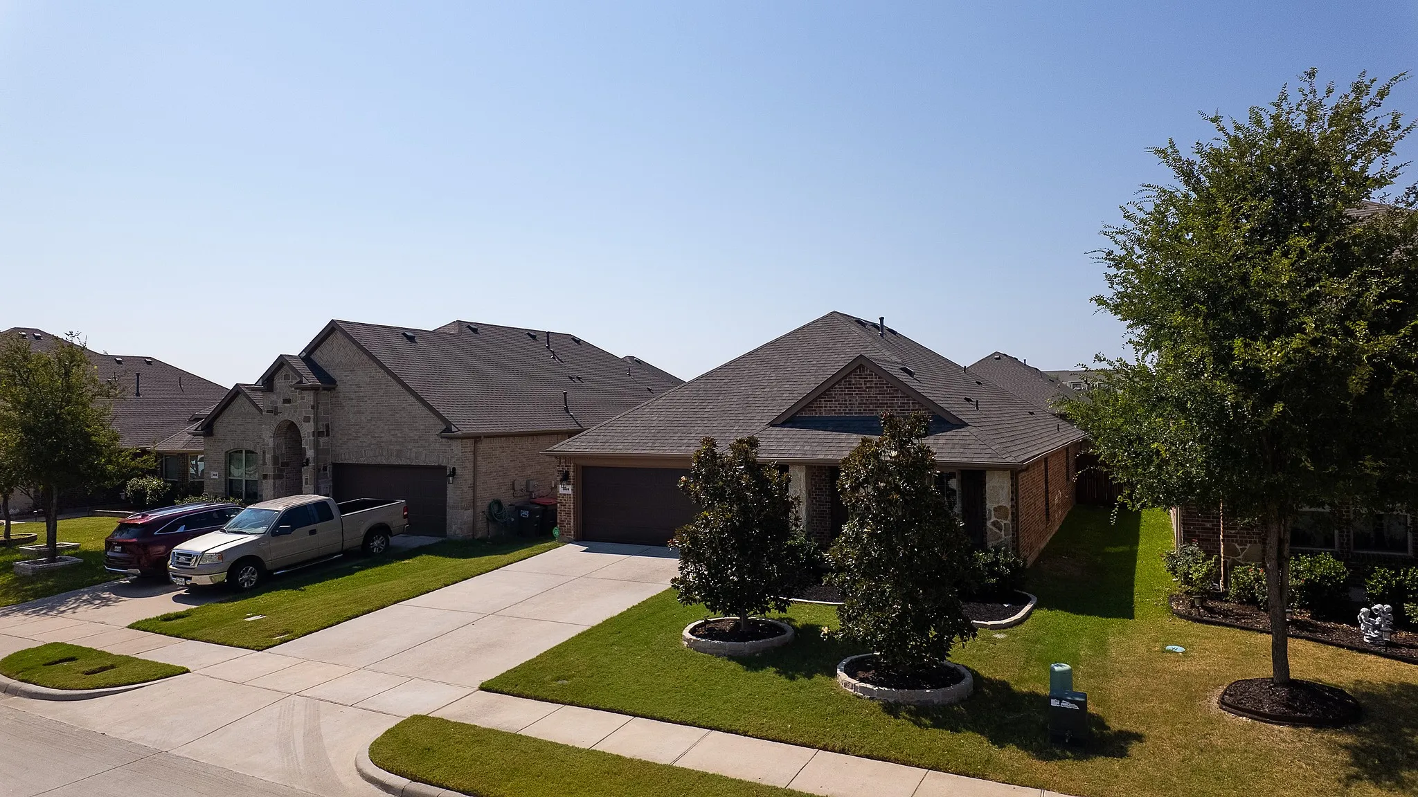Brick exterior home featuring a dark shingle roof, attached garage, concrete driveway, manicured lawn, and mature landscaping