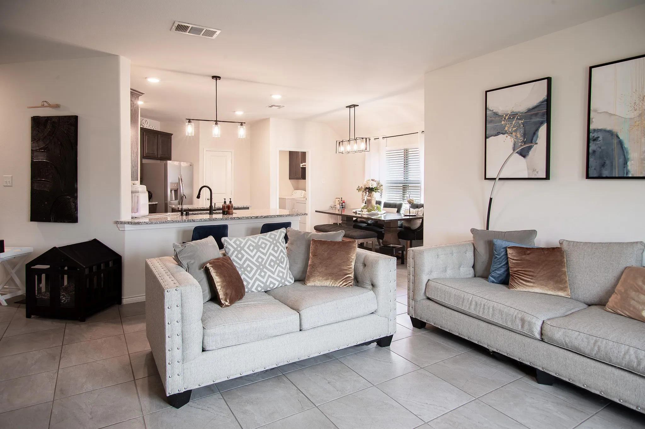 Open-concept living area featuring light-toned tile flooring, recessed lighting, and a modern kitchen with a breakfast bar and dark cabinetry