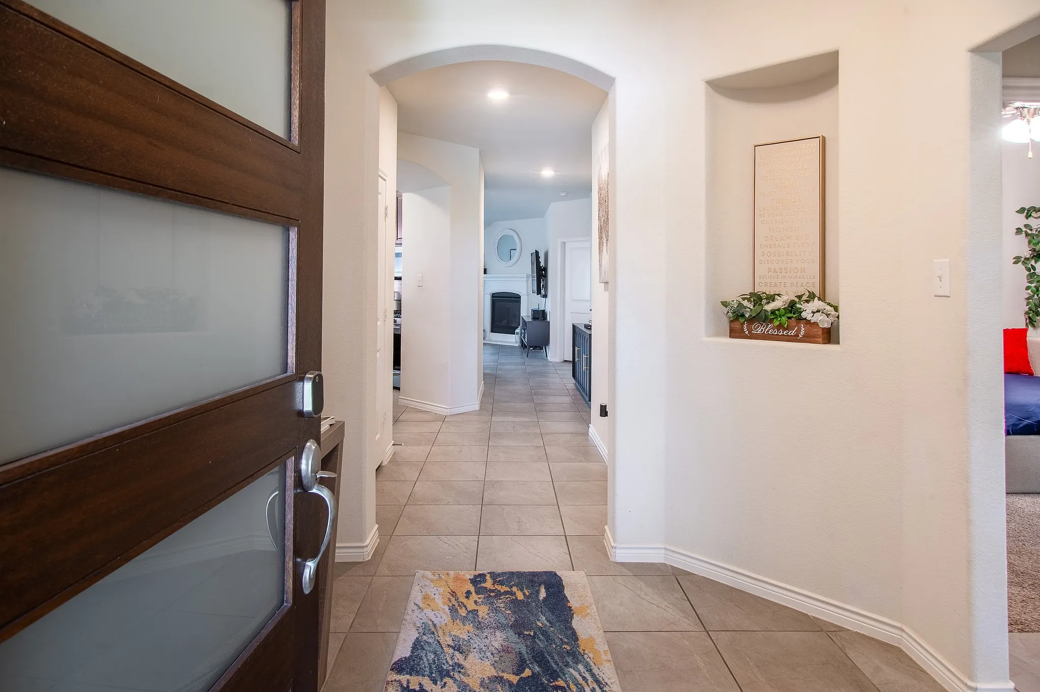 Entryway featuring a wood-finish door with frosted glass panels, tile flooring, an arched doorway, a recessed wall niche, and white baseboards