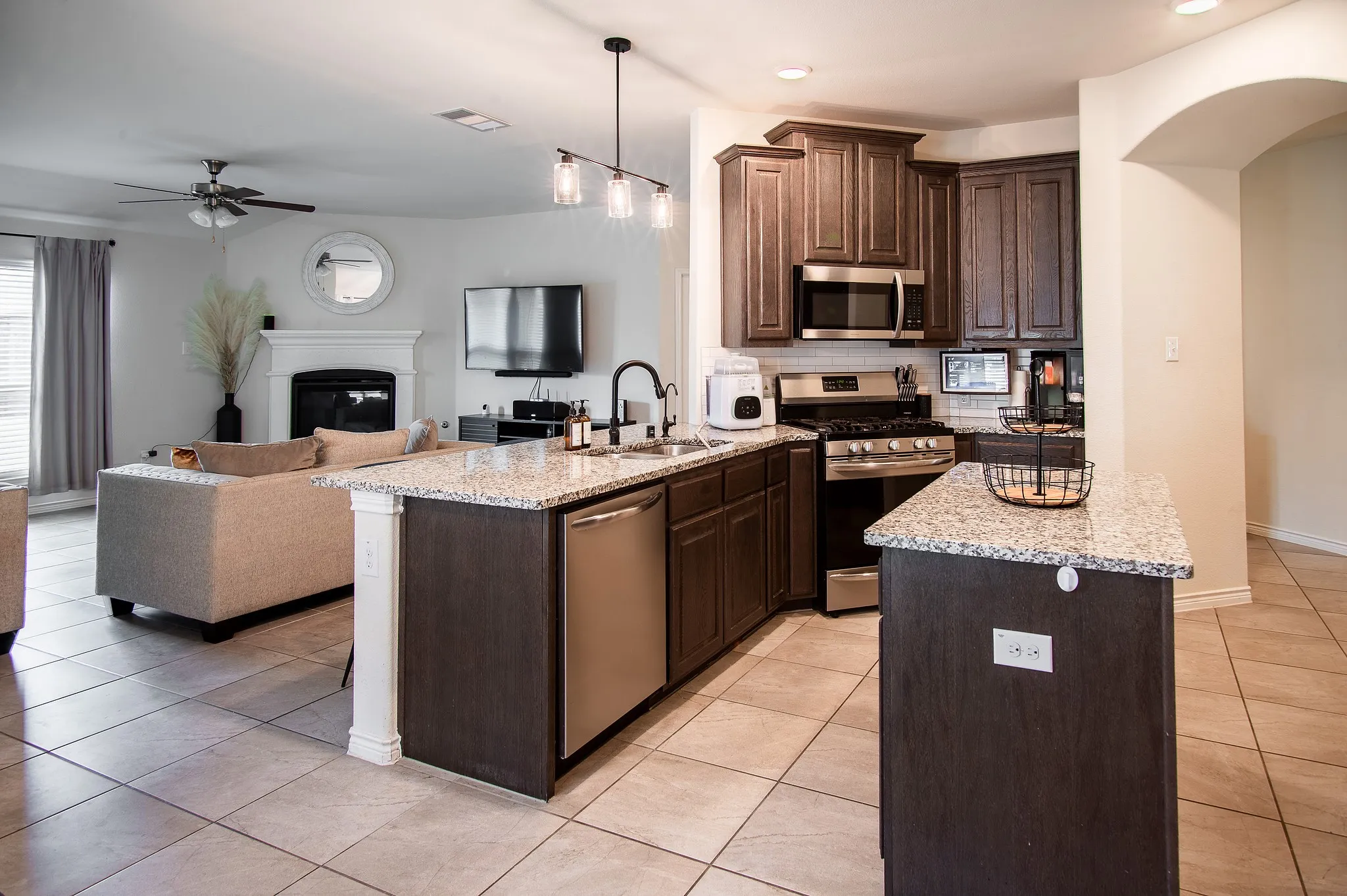 Open-concept kitchen featuring dark wood cabinetry, stainless steel appliances, granite countertops, and tile flooring