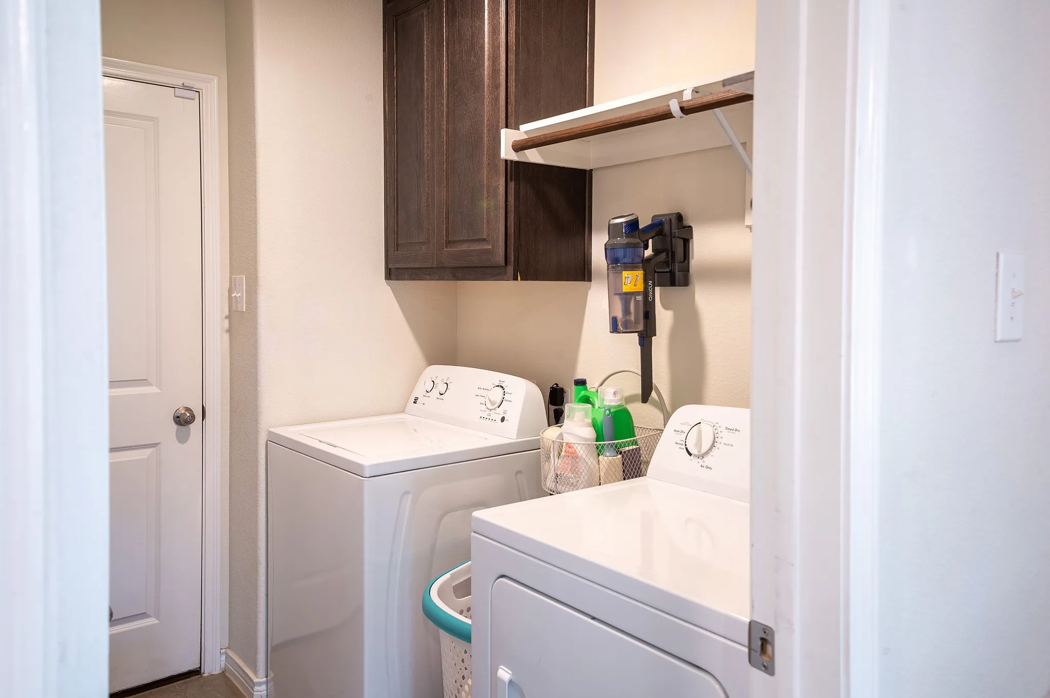 Dedicated laundry area featuring a white door, overhead dark wood-finish cabinetry, and a white shelving unit