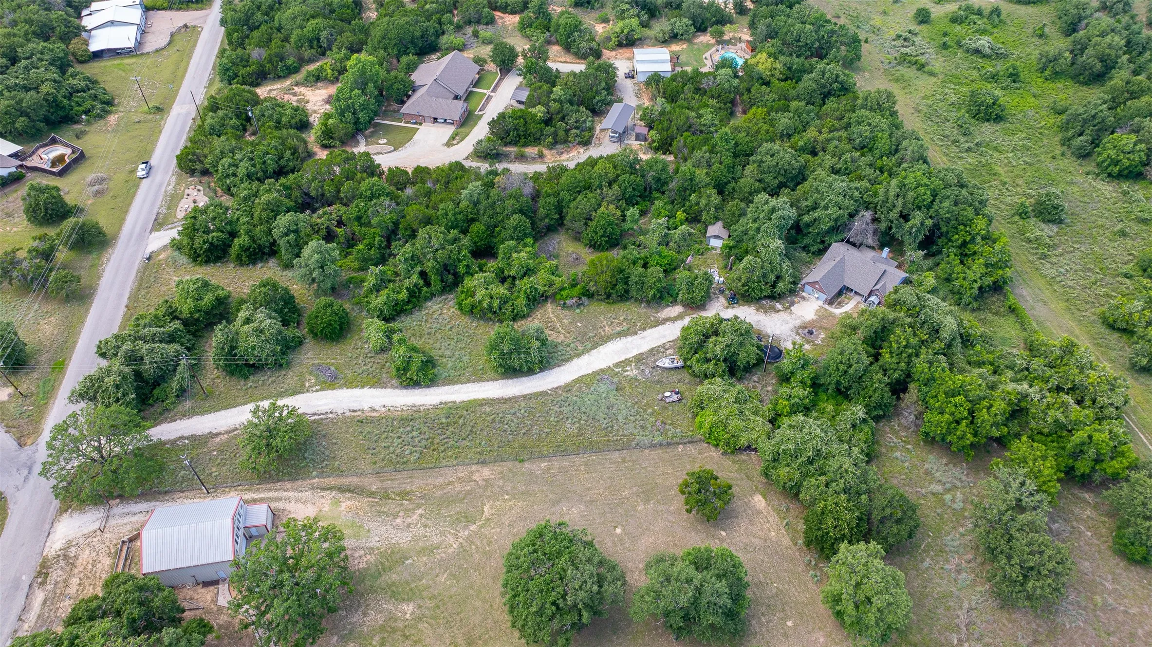 Expansive rural property featuring a main residence with a dark roof, surrounded by mature trees and natural landscaping