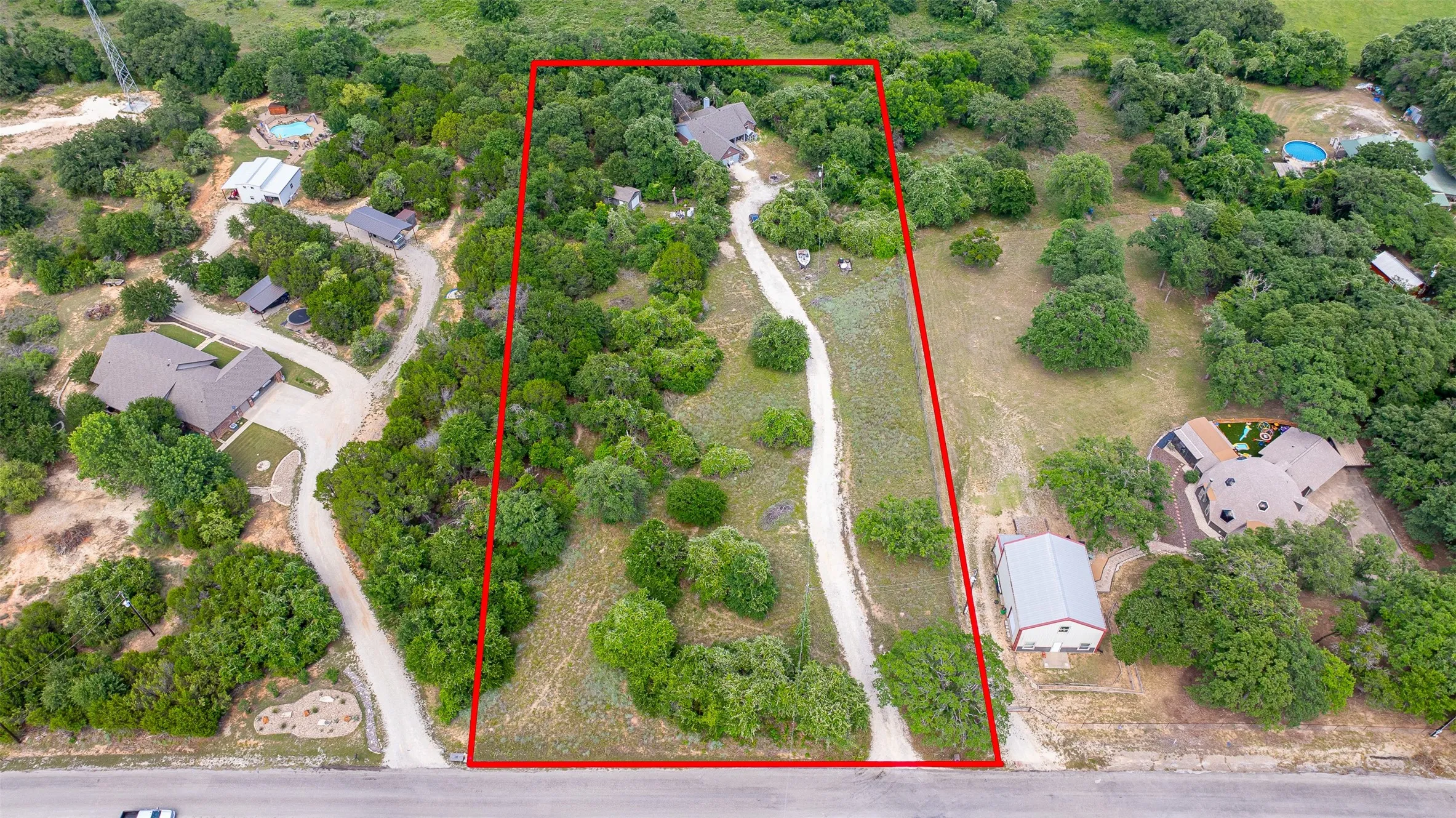 Expansive property featuring a gravel driveway, mature trees, and a combination of wooded and open land